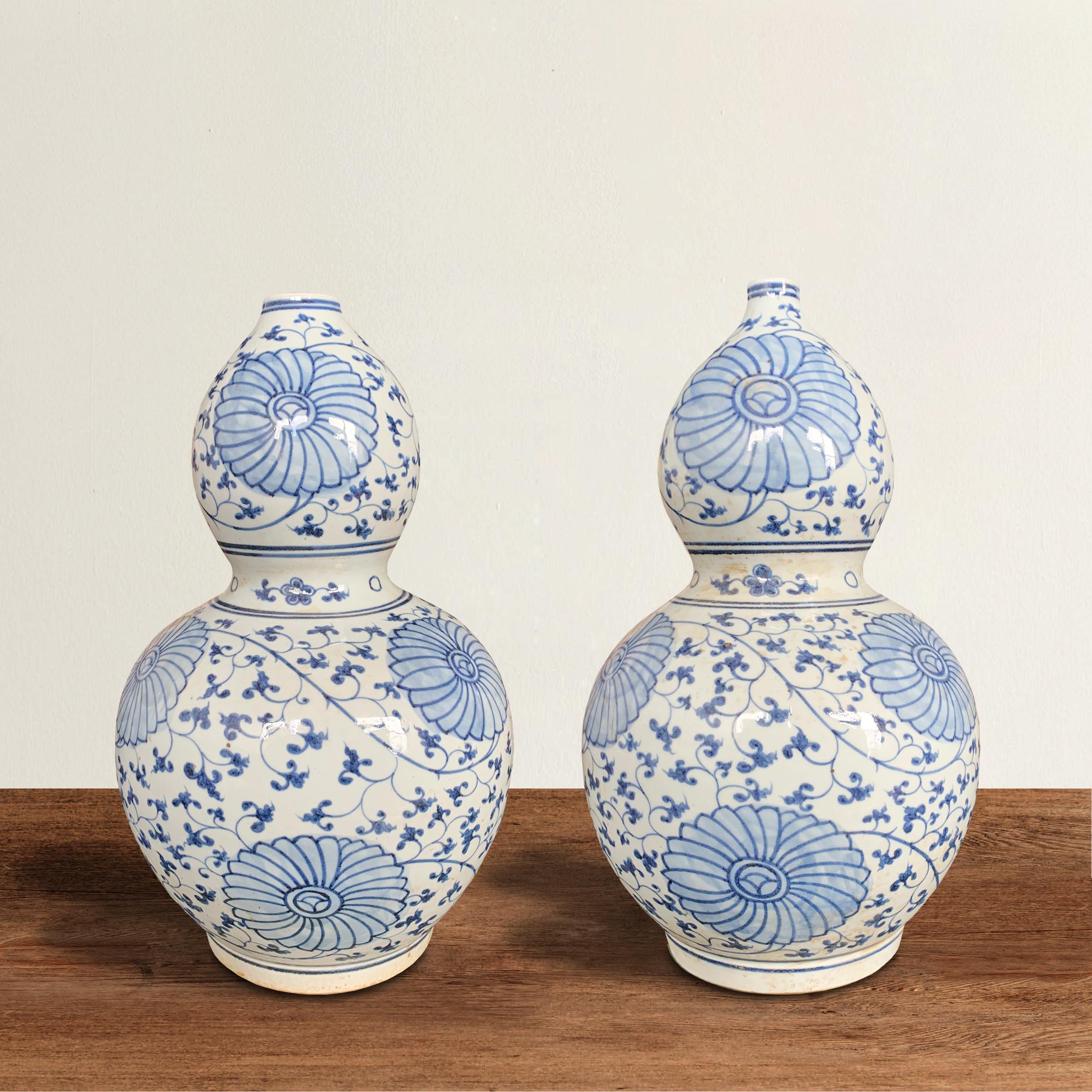 A wonderful pair of Chinese hand painted blue and white glazed porcelain double-gourd vases with a unique large scale floral and scrolling vine pattern.
