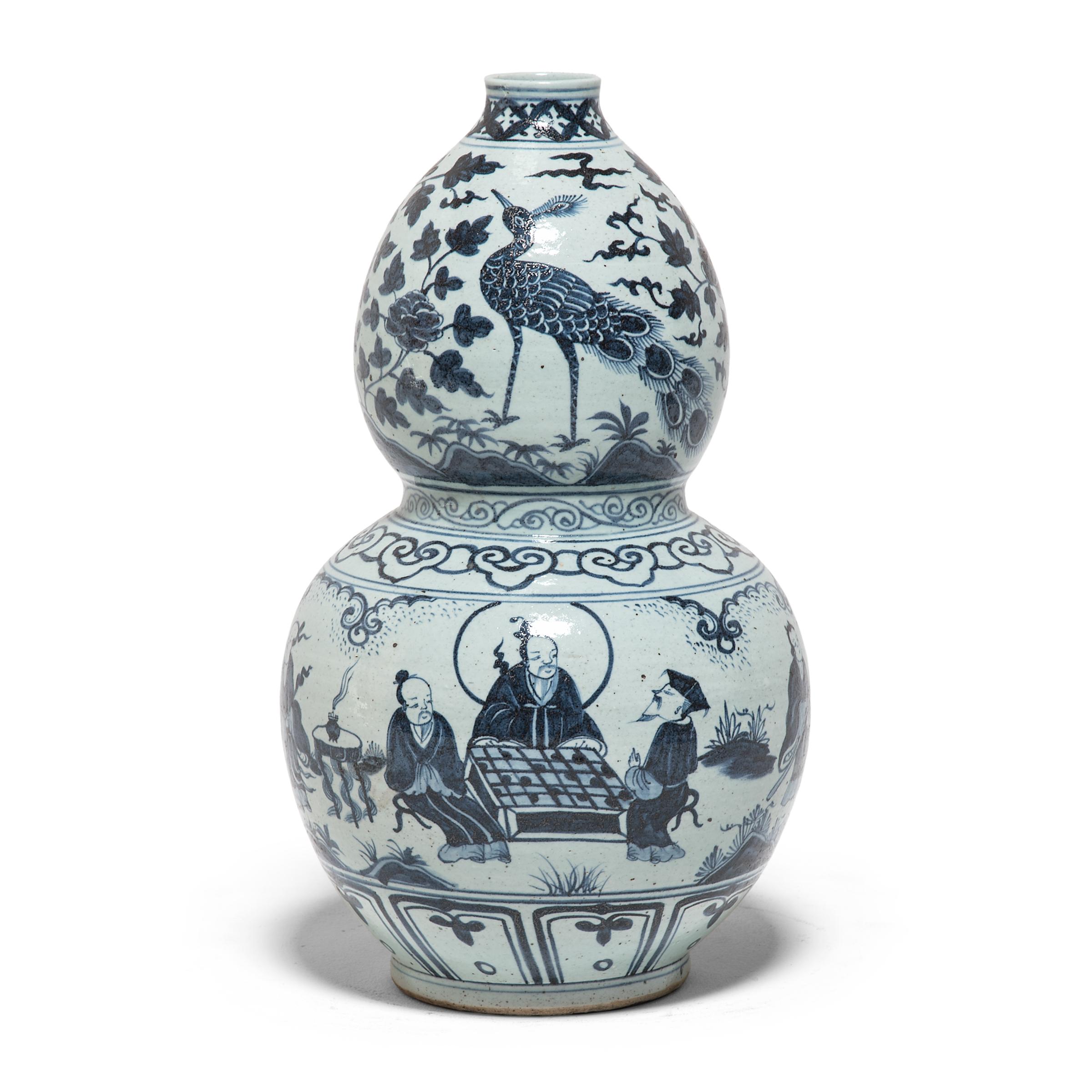 Working within the time-honored tradition of blue-and-white porcelain, artisans from China's Jiangxi province painted this pair of contemporary double-gourd vases with scenes from a wondrous scholar’s garden. Using the porcelain vessel’s hourglass