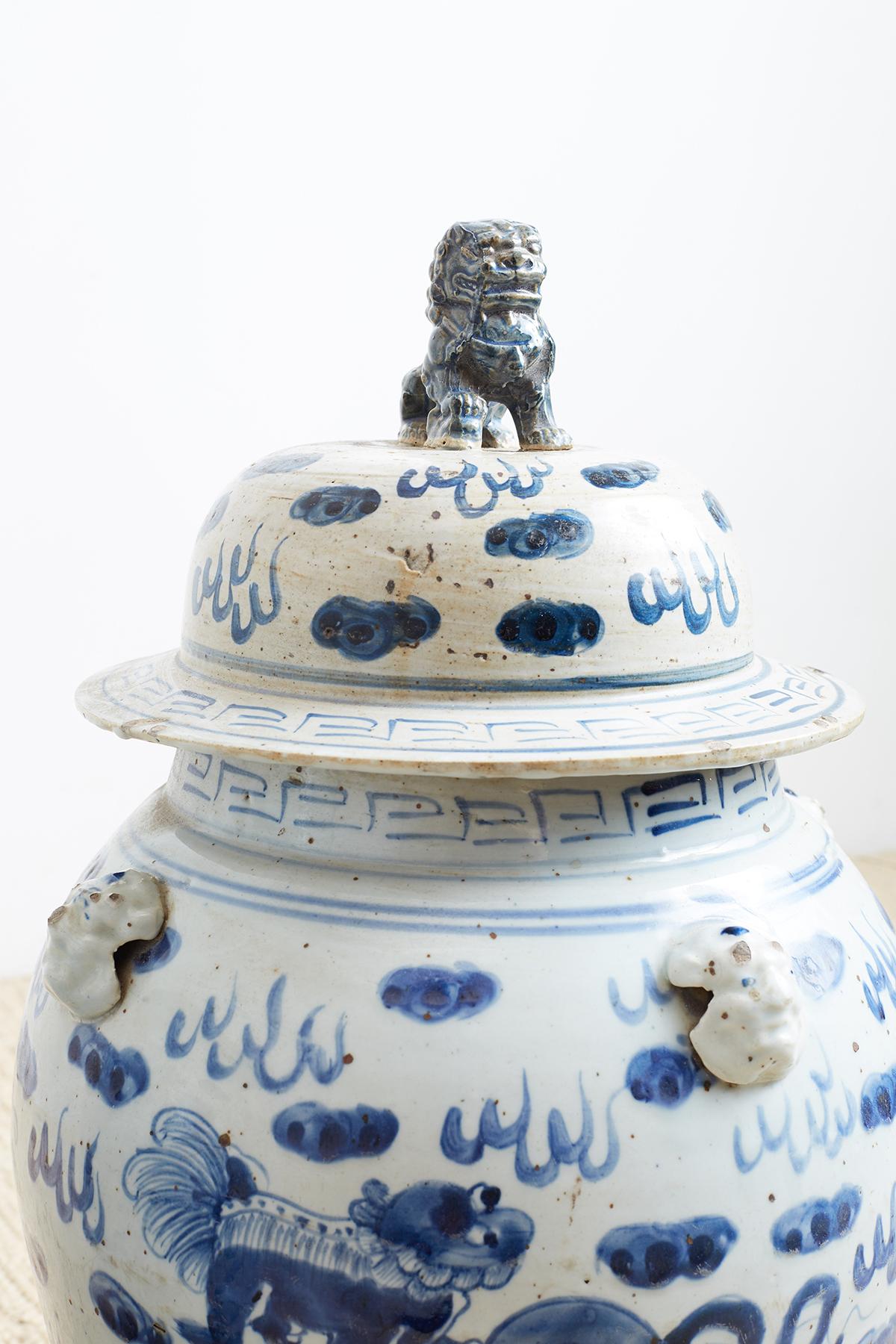 Large pair of Chinese blue and white ginger jars featuring painted foo dogs or lions amid whimsical clouds. Each jar has mythical beast heads on the shoulders. The matching lids appear to be original and have a large foo dog finial on top. Both have