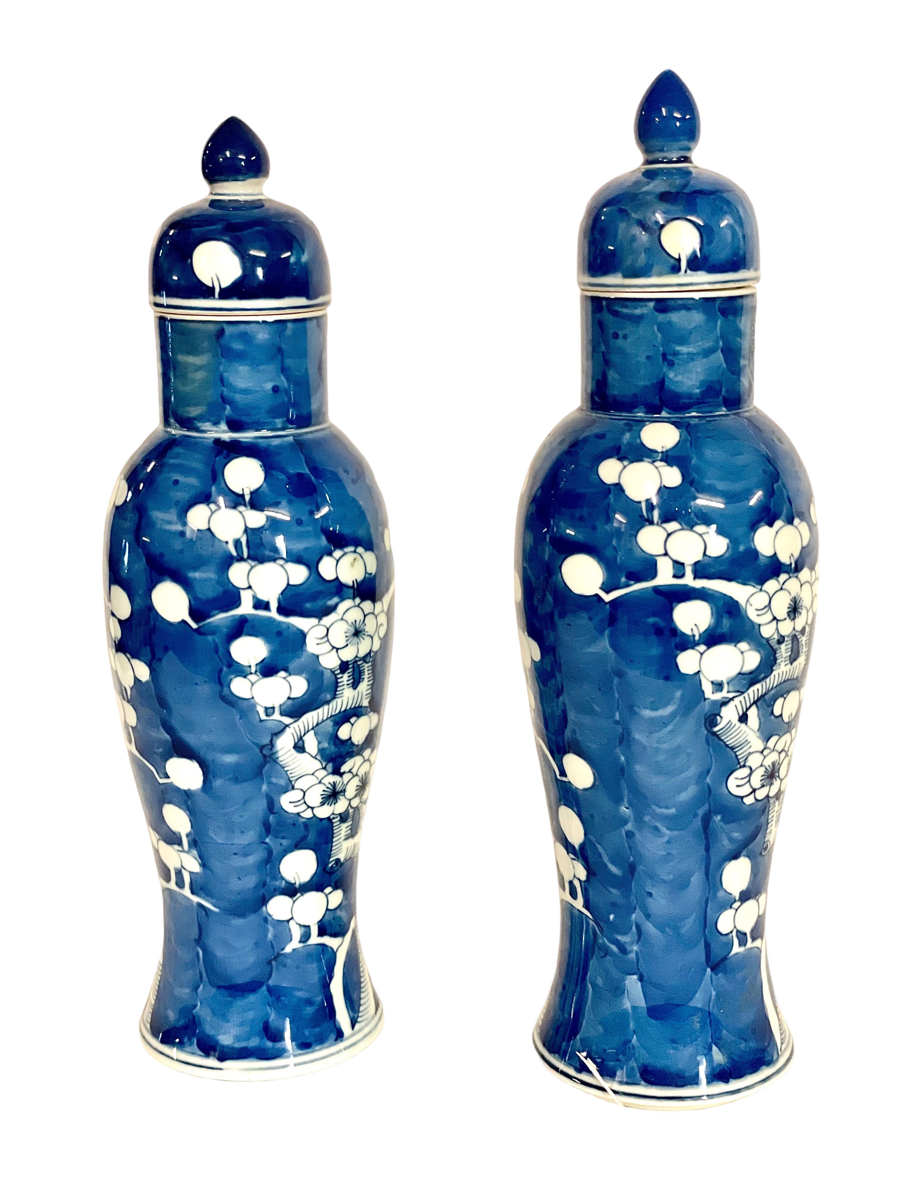 An exquisite pair of Chinese porcelain lidded vases, in baluster form and beautifully hand-painted with a traditional decoration of entwining branches of white blossoming prunus set against a deep blue background. The lids are close-fitting, with an