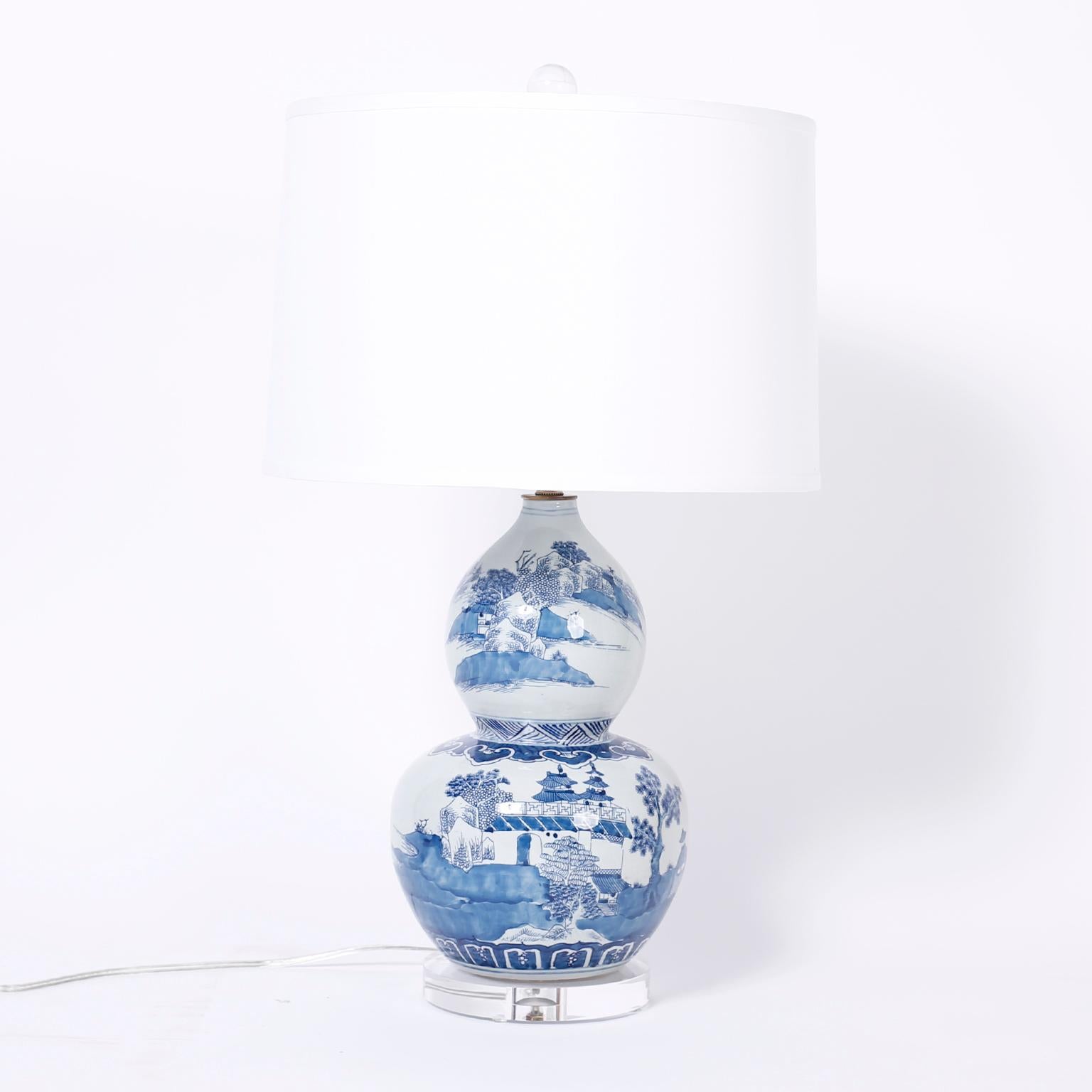 Dynamic pair of Chinese blue and white porcelain table lamps with a Classic double gourd form, hand decorated with architectural landscape and presented on Lucite bases.