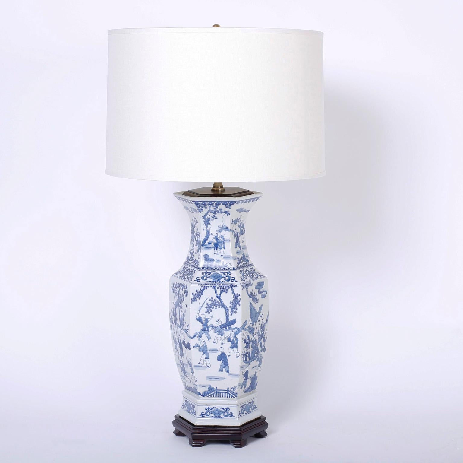 Pair of classic blue and white Chinese porcelain table lamps with a hexagon form hand decorated on all six sides with symbolic chinoiserie scenes and with a polished mahogany cap and base.