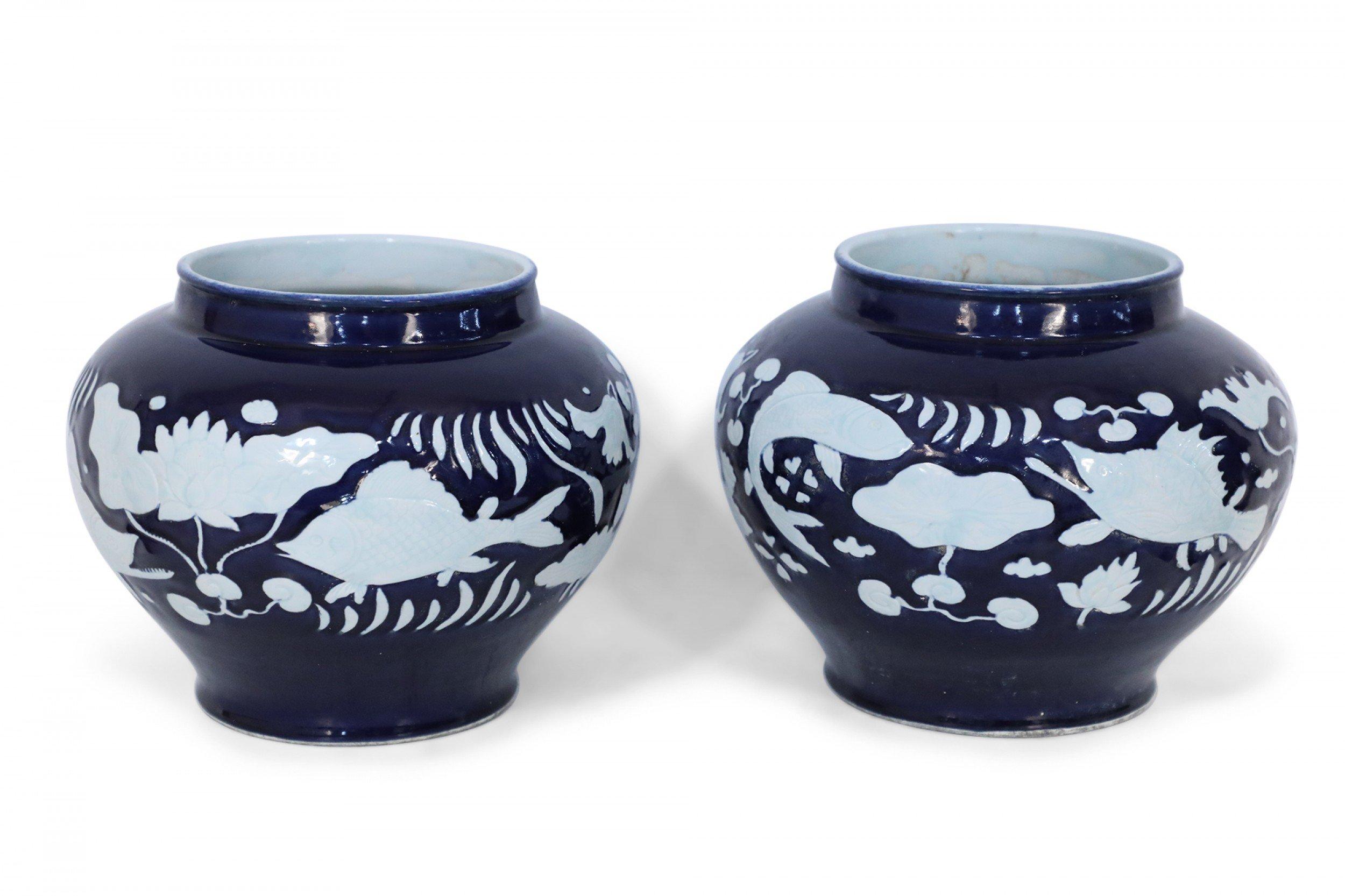 Pair of Chinese porcelain pots in dark navy hues decorated with white underwater motifs capturing the silhouettes of fish and vegetation (PRICED AS PAIR).
 