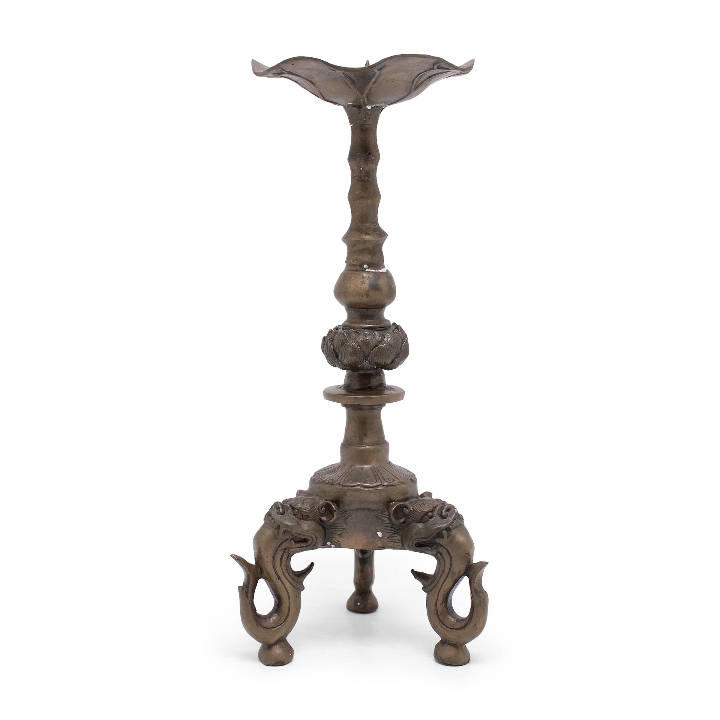 These brass candlesticks were cast with a fantastic sculptural form and are a beautiful example of Chinese metalwork. The scalloped candle dish is shaped like a delicate lotus leaf, floating above a lotus blossom shoulder and a tripod base. Each leg