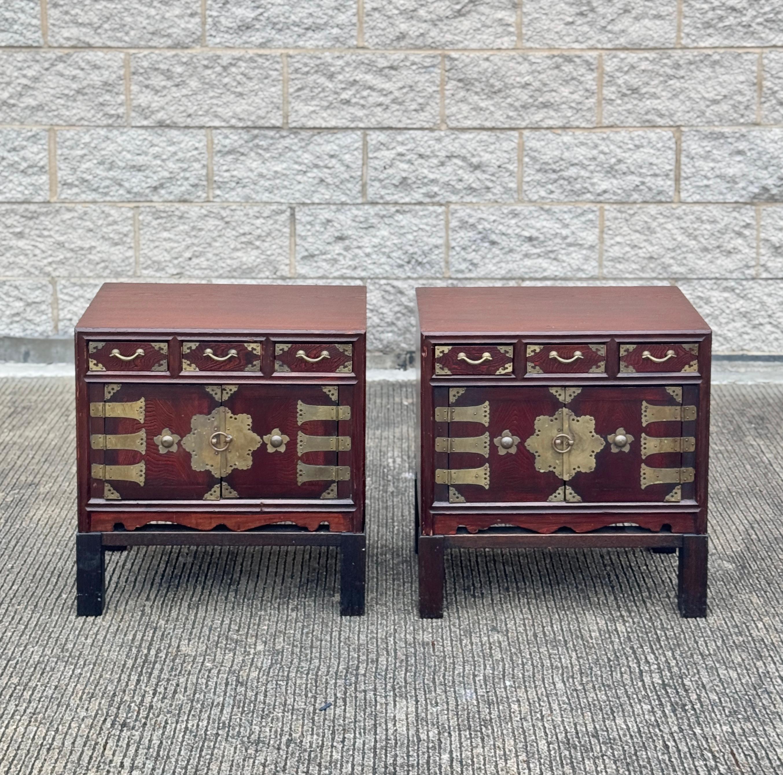 These vintage tansu style nightstands exude luxury with their burl wood construction and brass fittings. Versatile enough to serve as side tables, they feature multiple drawers and ornate doors revealing red fabric-lined compartments. Inspired by