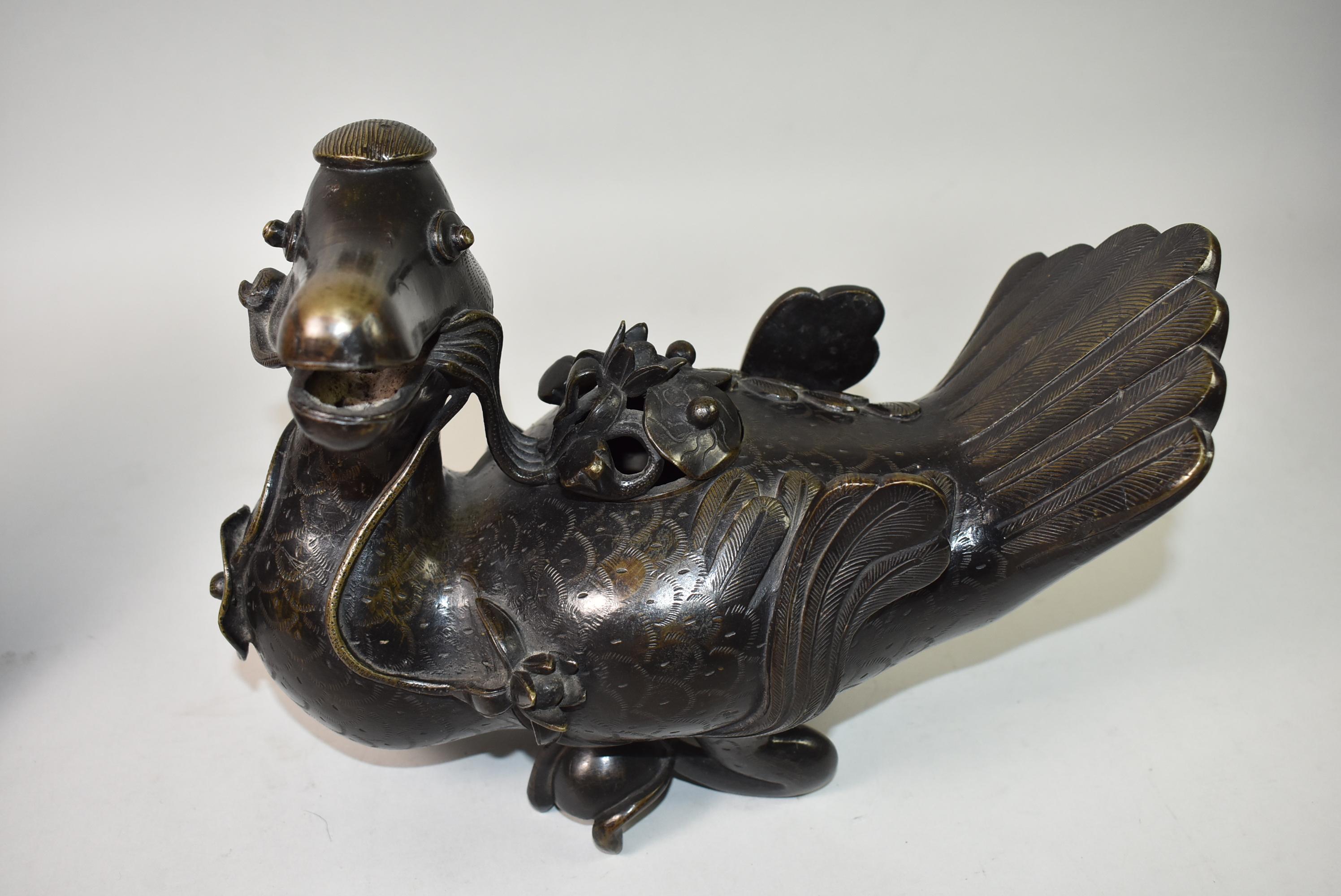 This pair of Chinese bronze mandarin duck form censors with lids are cast in a mirror image of each other, with upswept details on the wings and tails. The heads are turned to the side with lotus flowers in their open beaks. The domed covers are