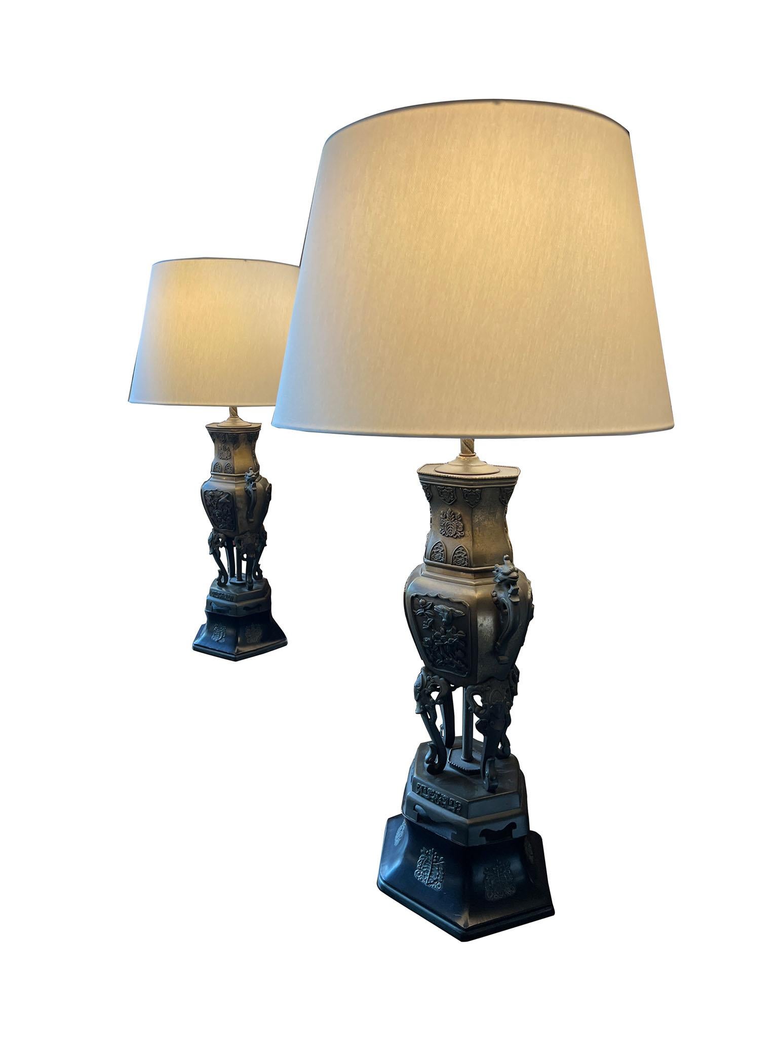  Impressive pair of Chinese bronze table lamps in the style of influential 20th Century American furniture designer James Mont. The lamps, crafted in oil rubbed bronze, resemble traditional Chinese urns atop hexagonal pedestals. Two dragons sit as