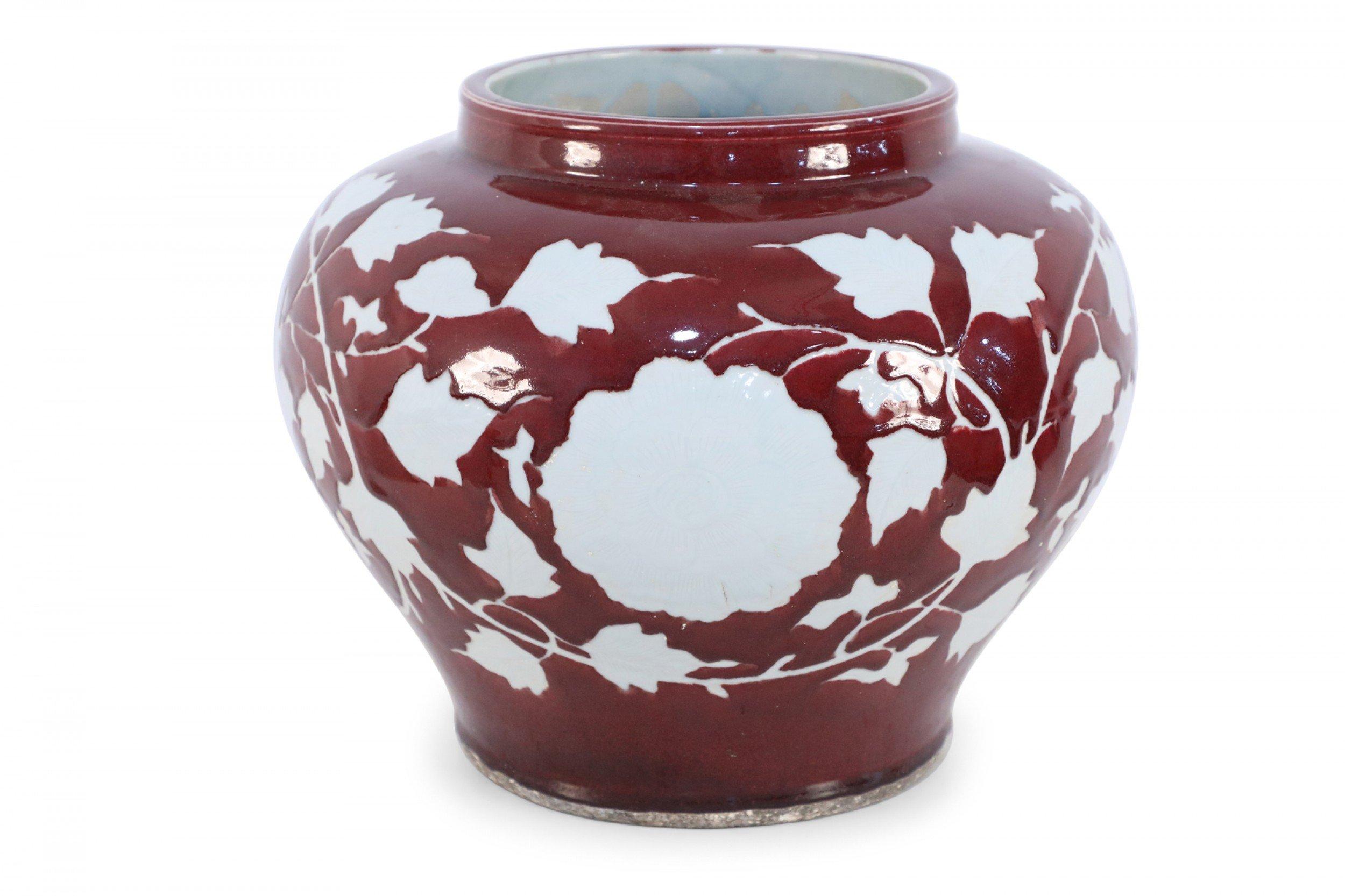 PAIR of Chinese ceramic burgundy pots decorated with white floral motifs capturing the silhouette of florals, vines and leaves surrounding central medallions (PRICED AS PAIR).

Condition: Good; Wear consistent with age and use