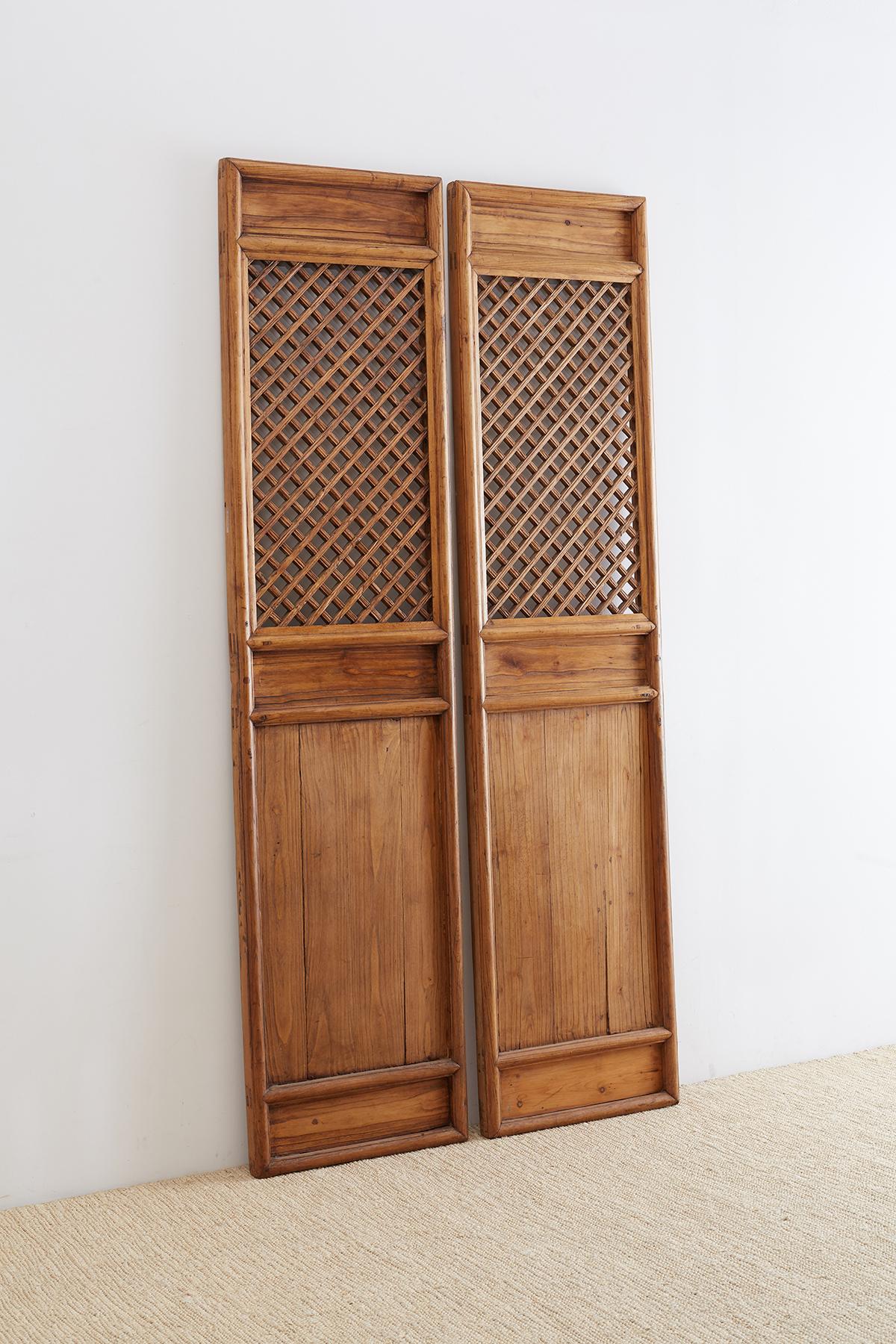 Large pair of Chinese hand carved door panels featuring lattice windows. Beautifully constructed from elm with mortise and tenon joinery. Each window has a geometric fretwork of interlocking pieces and the doors have deep recessed panels. The doors