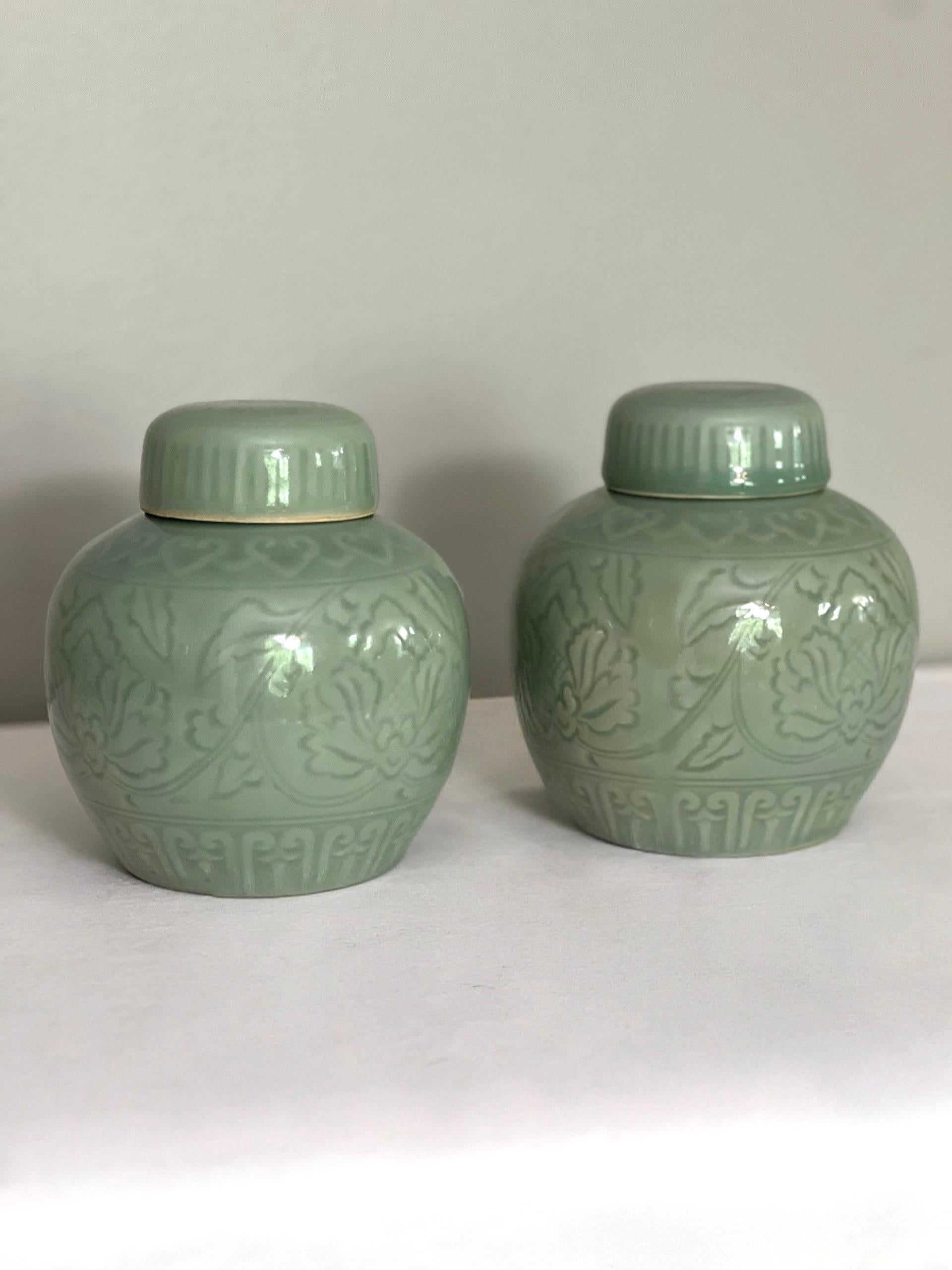 Vintage 1960s pair of Chinese celadon lidded ginger jars.  They display lovely form with incised lotus and decorative trim patterns topped with a domed lid with a floral medallion while the soothing blue-green celadon brings a beautiful touch to a