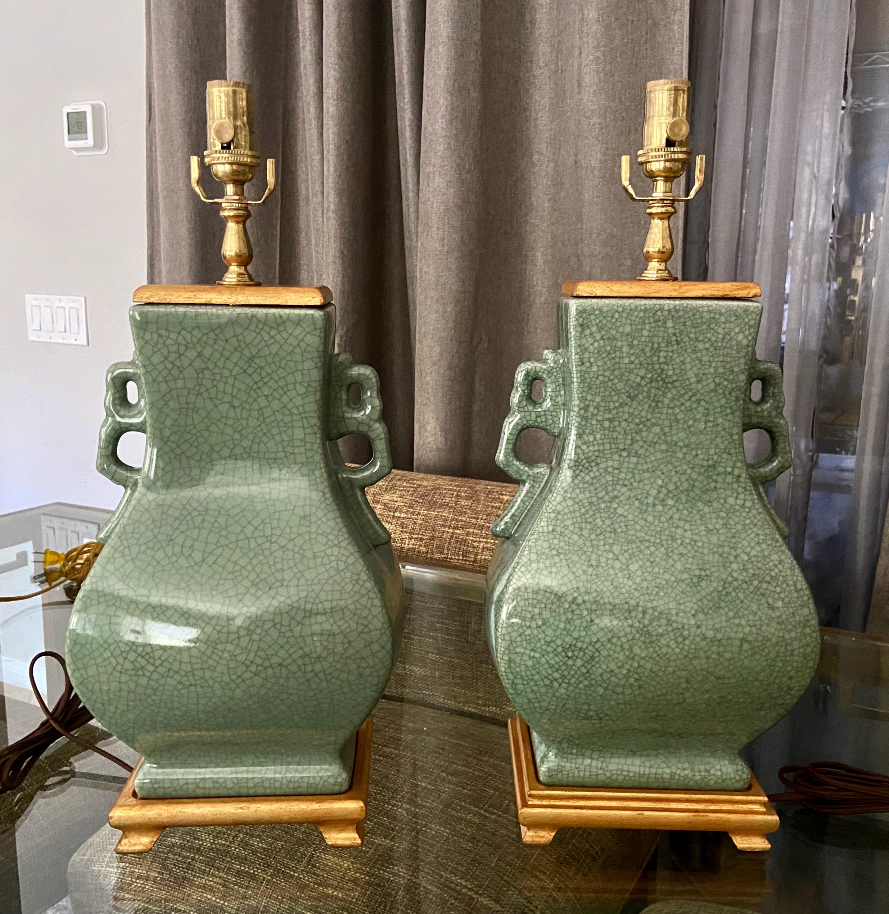 Pair of Chinese Asian celadon green crackle glaze porcelain table lamps with handles. Each mounted on giltwood bases along with matching vase cap. Newly wired with new 3 way brass sockets and rayon cords. The rectangular shape measures 22