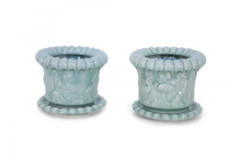 Pair of Chinese celadon colored pots with scalloped tops and detached base trays framing tonal, raised carvings of cranes in natural settings (priced as pair).
  