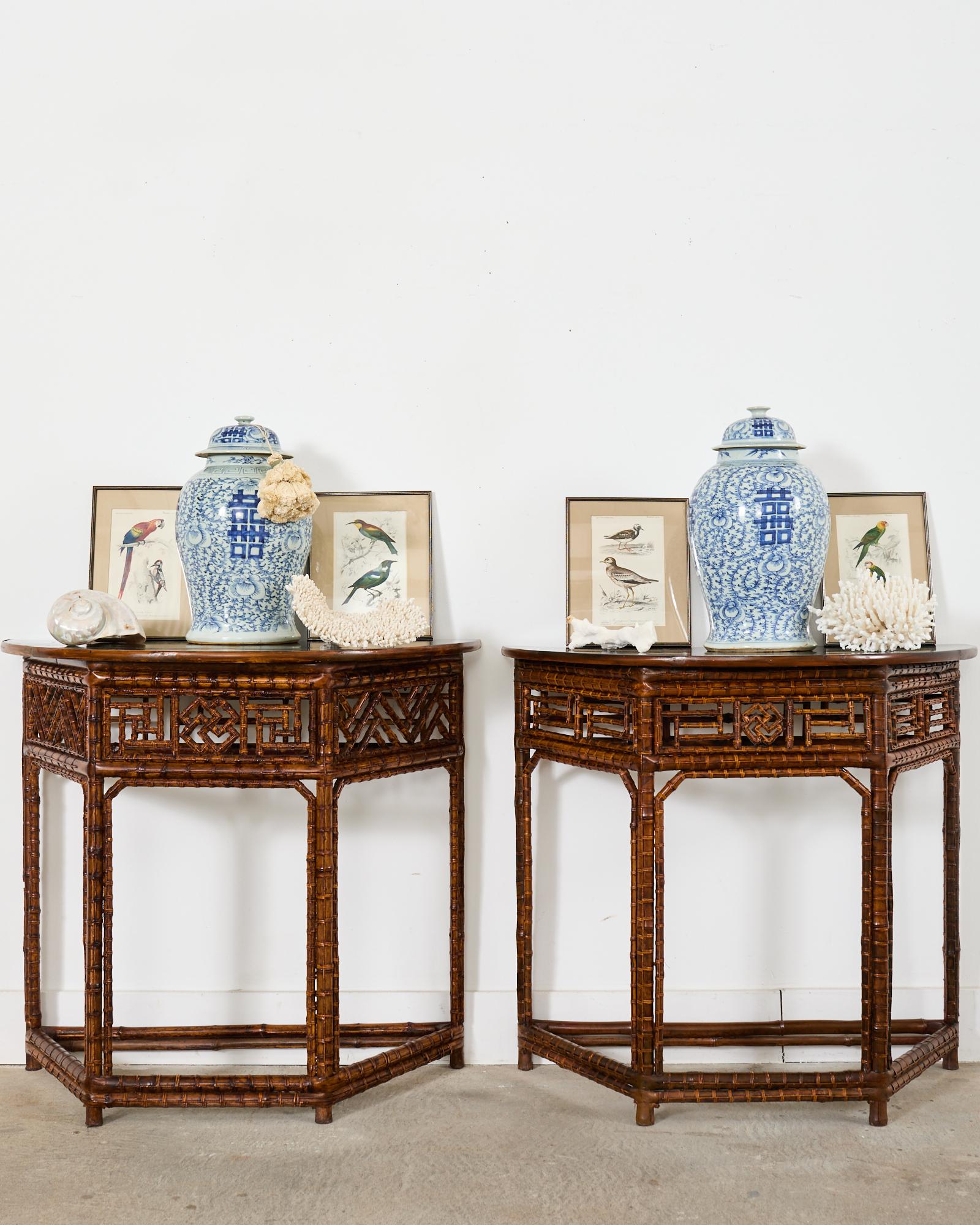 Dramatic pair of bamboo demi-lune console tables made in the Chinese Chippendale style. The tables feature intricate open fretwork designs that slightly vary on each table. Each table has a black ebonized lacquered top with a split bamboo edge. The
