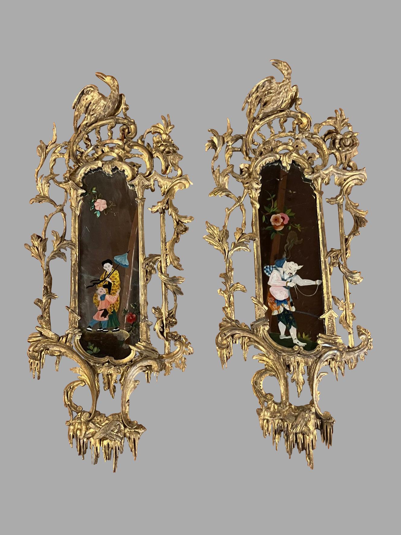 Un par muy bonito de girándulas inglesas de estilo Chippendale chino, cada una de ellas crestada con un águila bien tallada que descansa sobre un estilizado marco foliado. Los espejos están decorados  una con la figura de una mujer y su hijo, la
