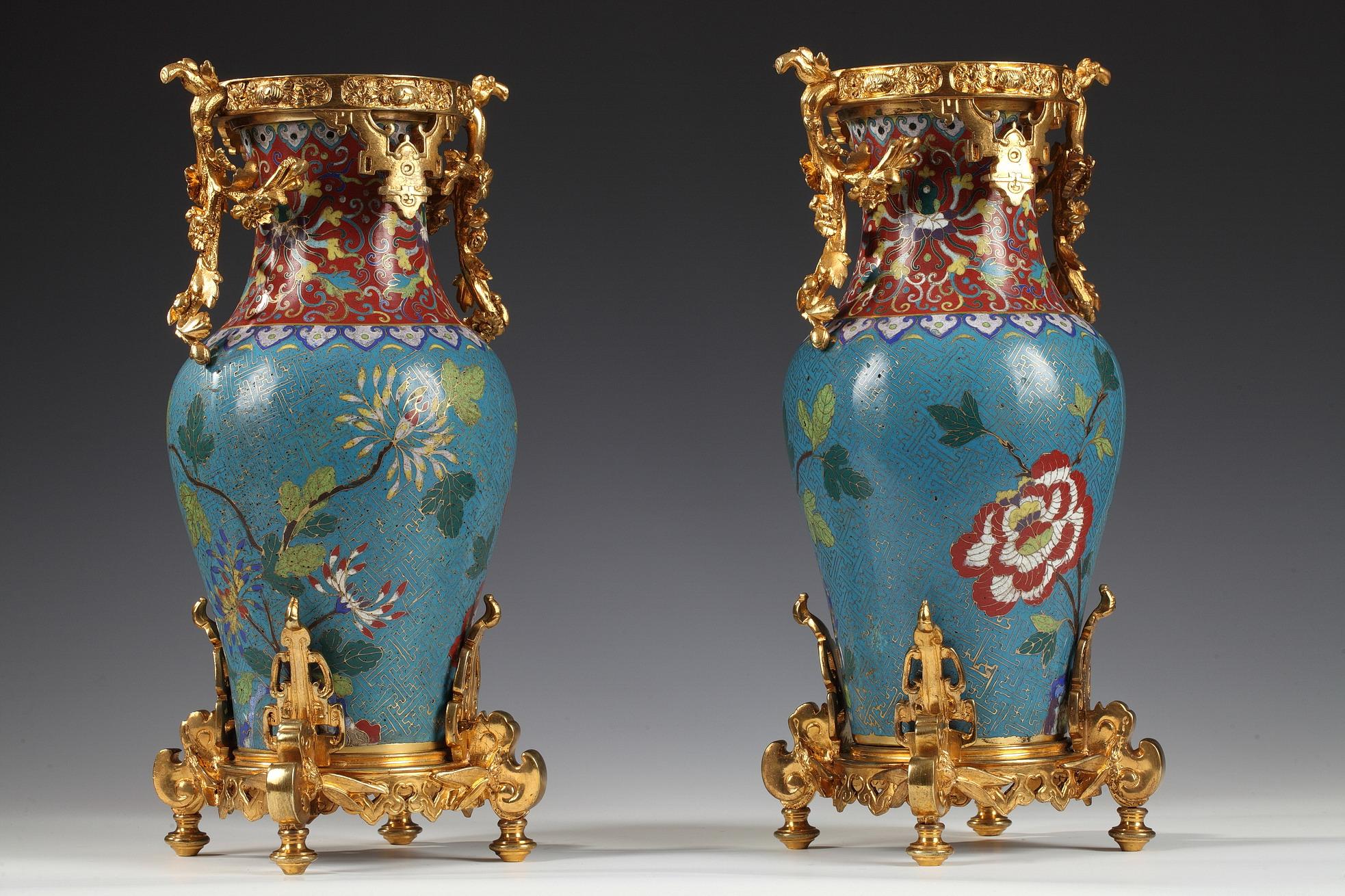 Elegant pair of Chinese cloisonné enamel vases in a gilt bronze mount attributed to the Escalier de Cristal. The vase is decorated with polychrome flowers and geometric gilded ornaments on a blue ground, and the neck with volutes on a red ground.