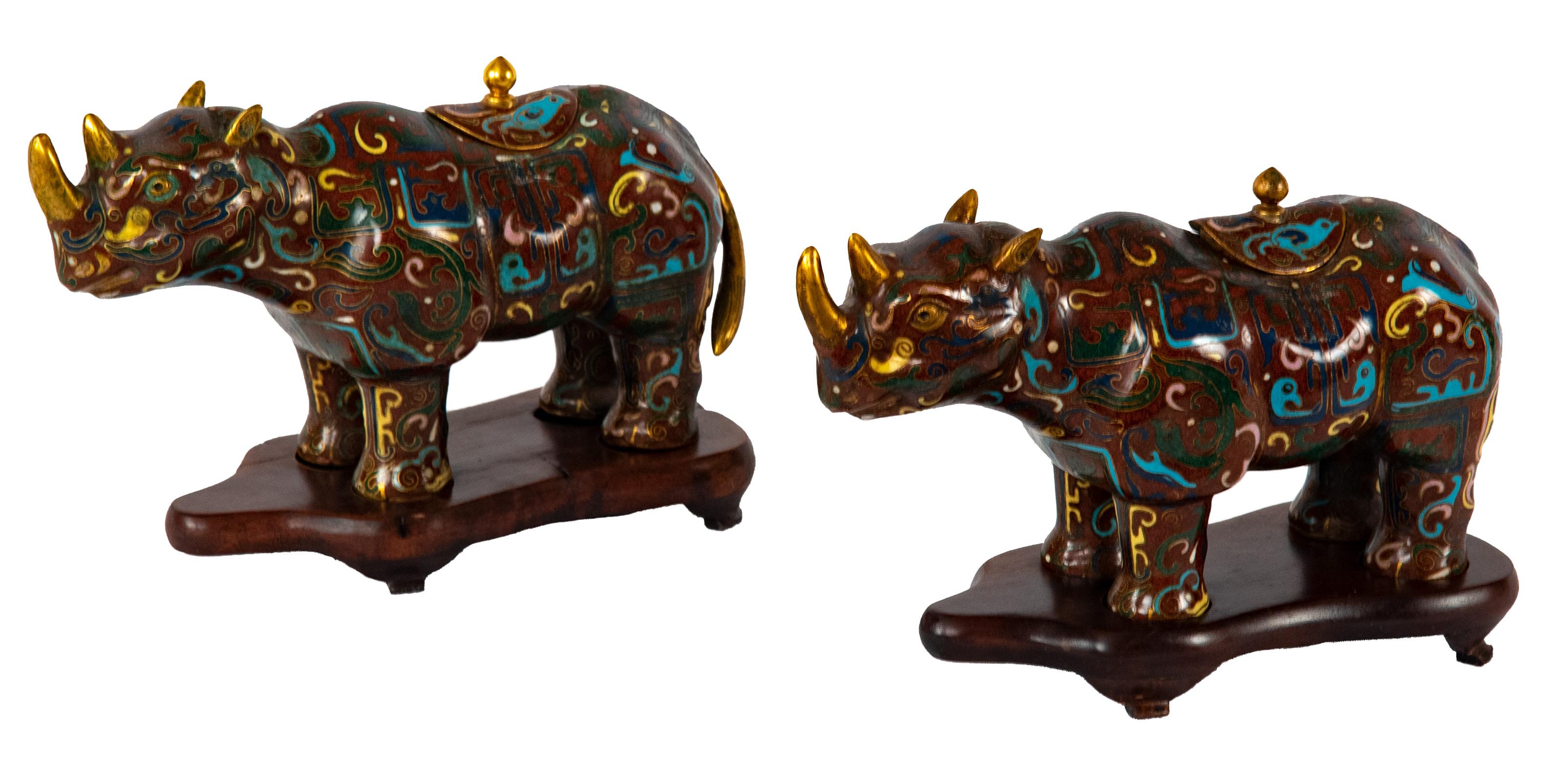 This pair of water pots in the form of standing rhinoceroses would have been made for the scholar's desk. Both are decorated with colorful patterns on an earth-red background; the brass of the horns, ears, and lid knobs are polished.