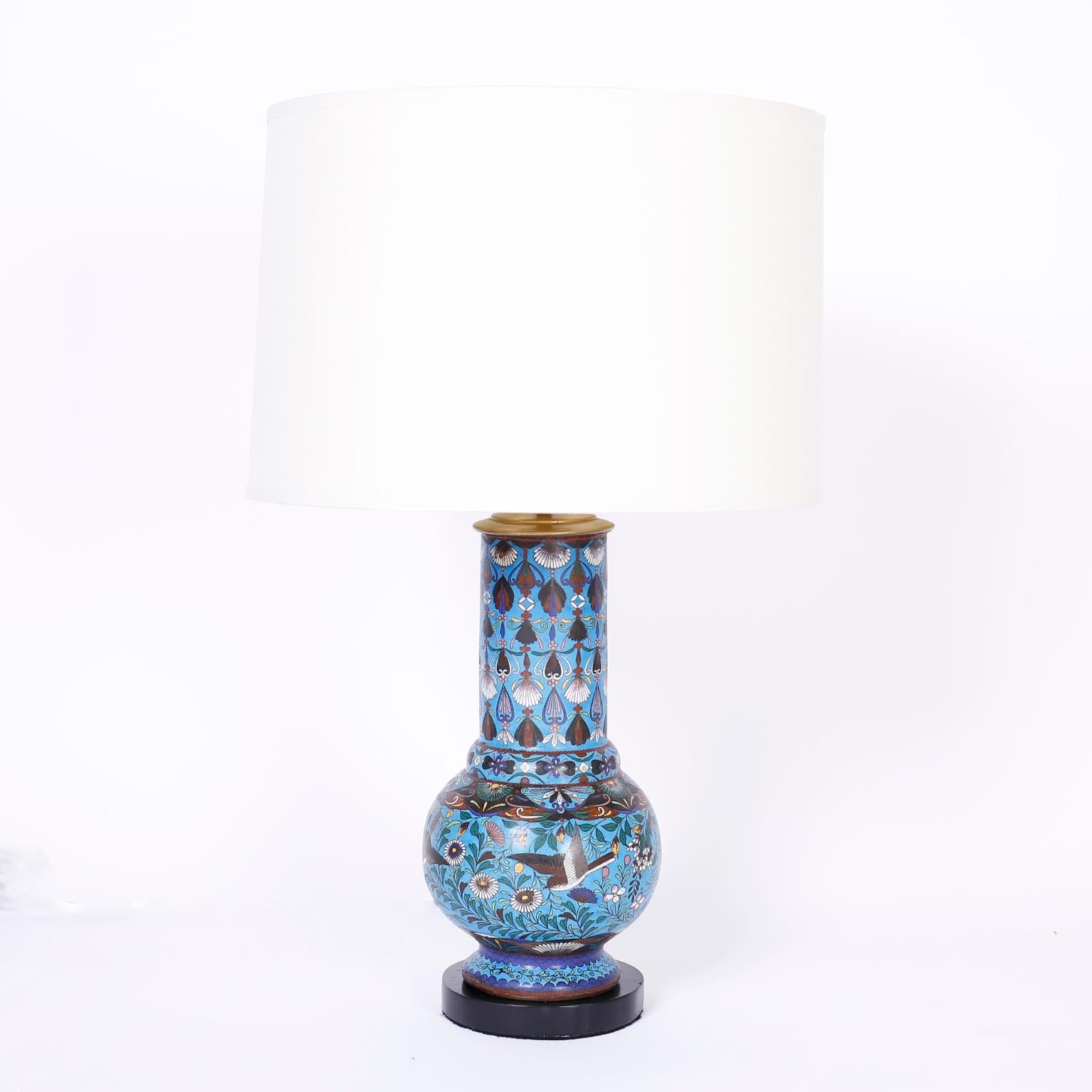 Pair of Chinese cloisonné table lamps expertly crafted with enamel on copper, decorated with birds and flowers over an alluring blue field and presented on ebonized wood bases.
