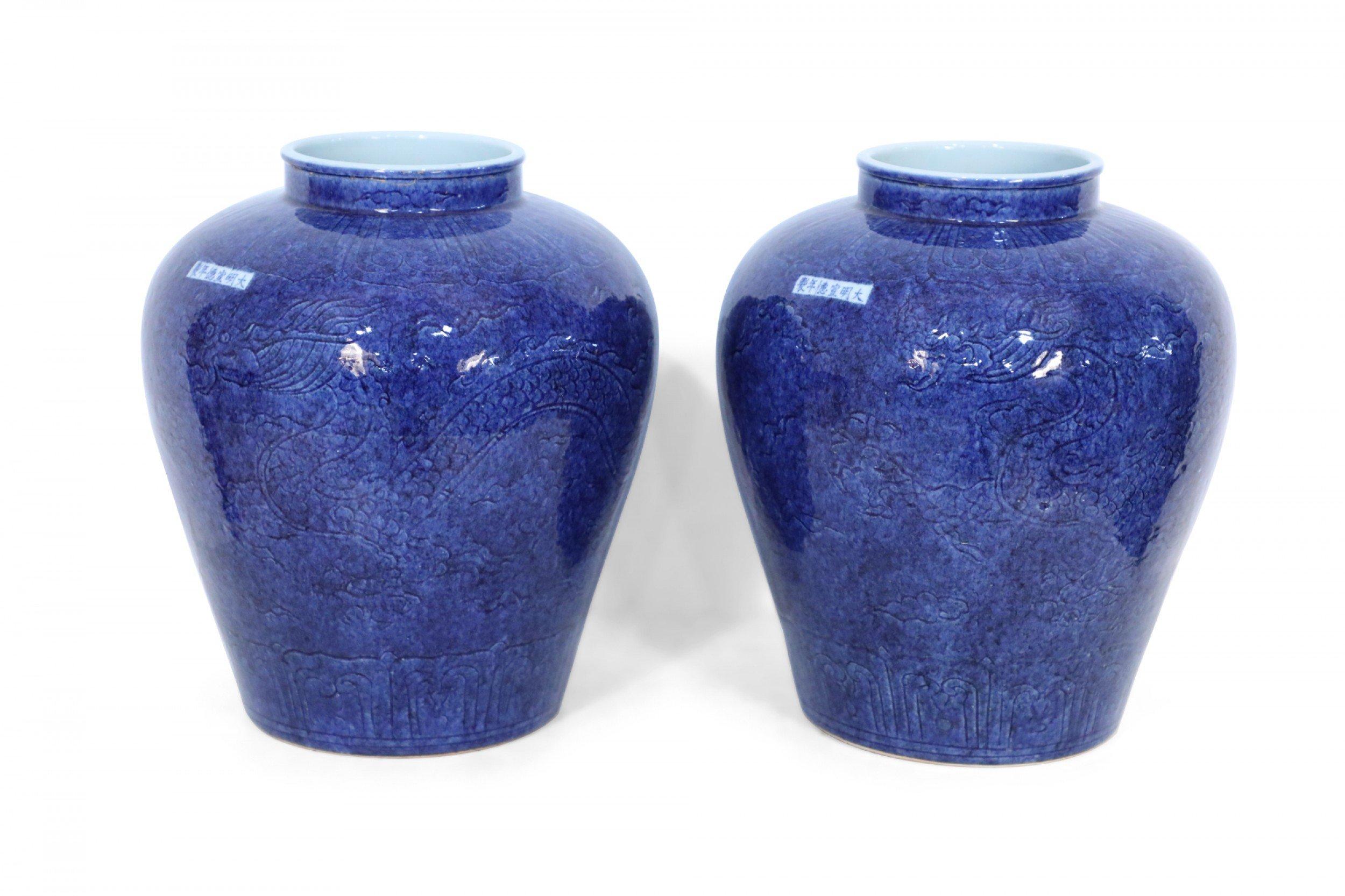 Pair of Chinese cobalt blue vases in ginger jar shapes, covered with incised patterns of dragons and curvilinear designs, and bearing small white rectangles featuring blue characters (priced as pair).
  