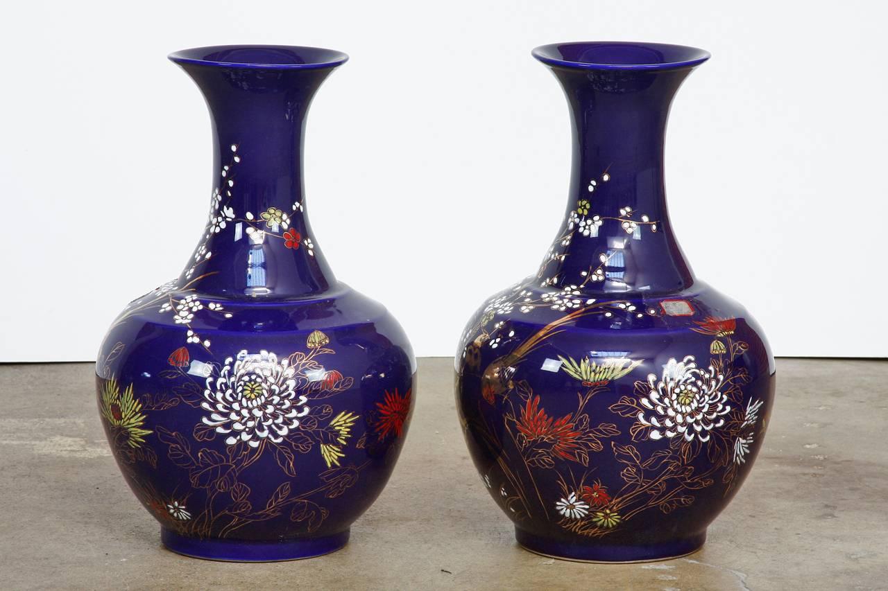 Colorful pair of Chinese cobalt blue glazed trumpet neck vases. Featuring flora and fauna decorated bodies. Bursting with bright colors and gilt decoration. Each having a Qianlong mark of the bottom, but from the late 20th century. Beautiful bulbous