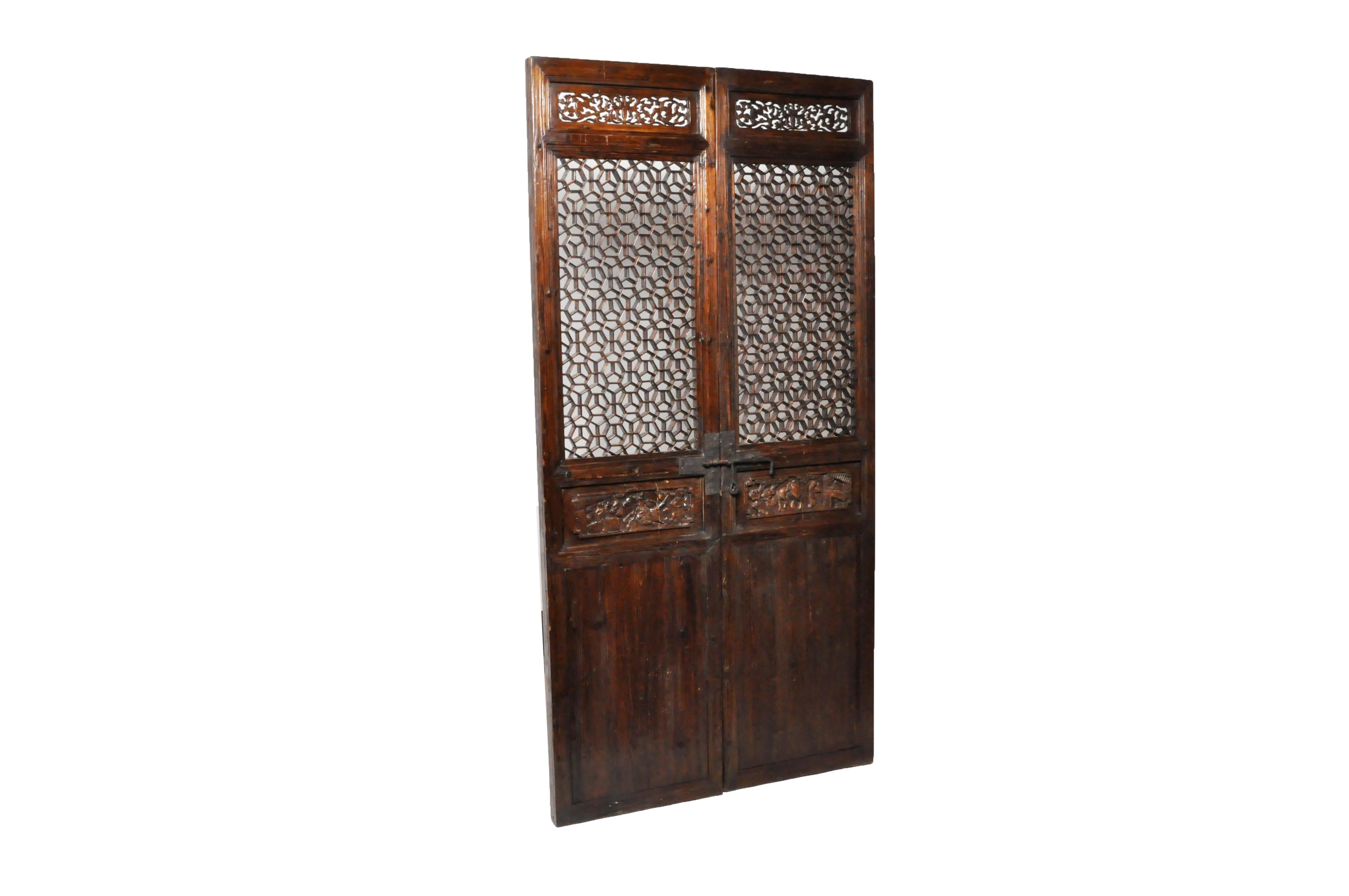 These elegant doors were once part of a large set that surrounded a courtyard in a Northern Chinese house. They feature fine latticework in a honeycomb pattern and carved details depicting courtly life. The deeply weathered and eroded surface of the