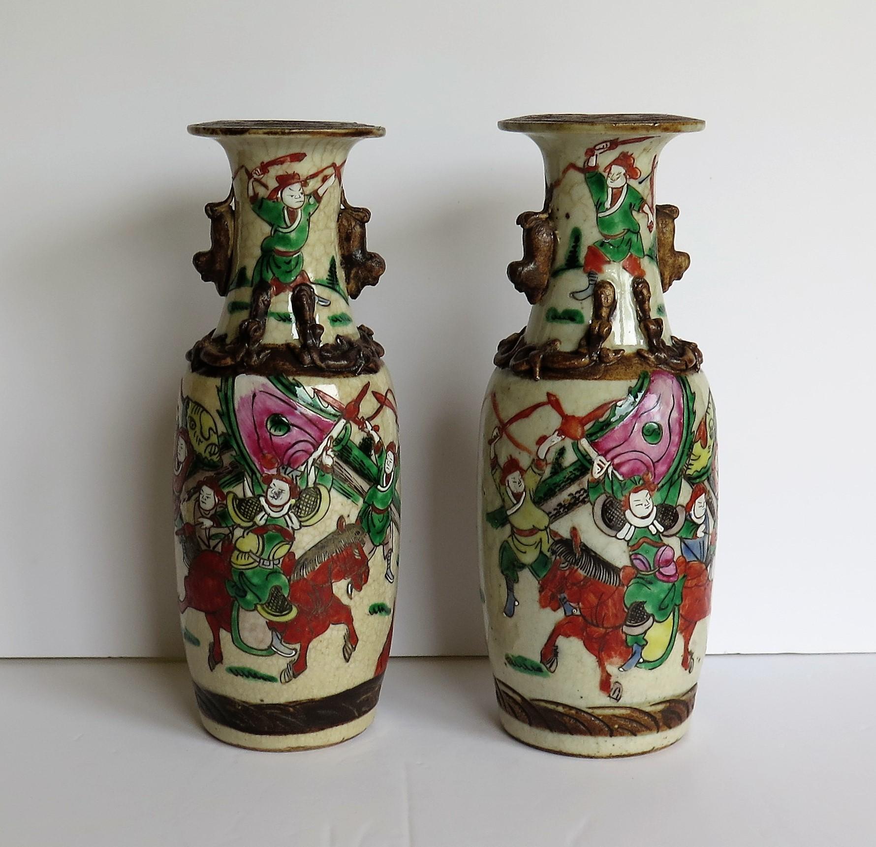 This is a good pair of Chinese crackle glaze ceramic vases with hand painted warrior scenes dating to the late 19th century, circa 1900.

Both vases have a baluster shape with a flared rim and are embellished to the neck with two foo dog handles and