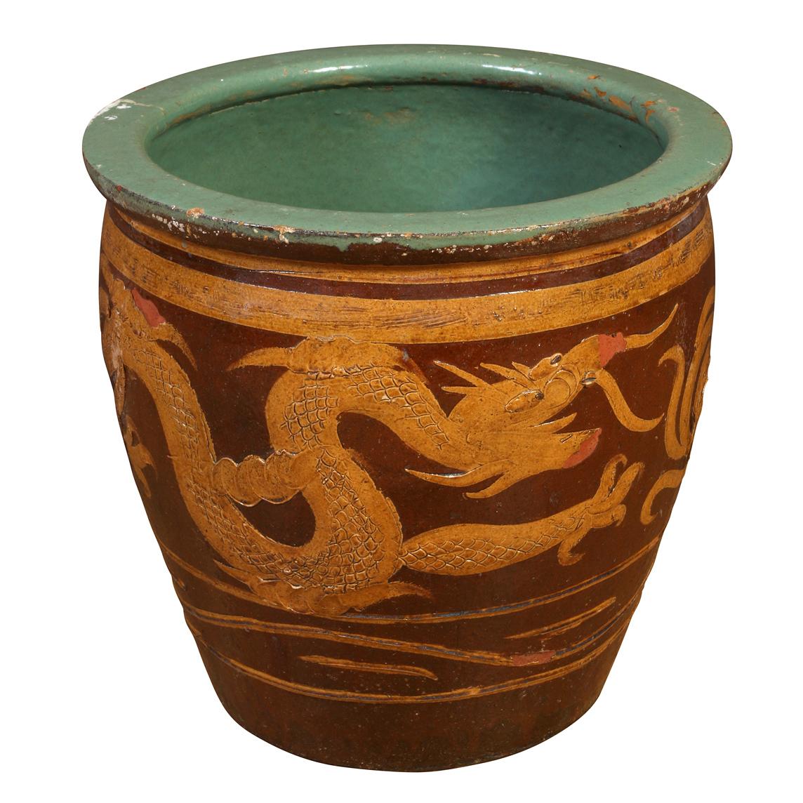 A pair of ceramic jardinieres with a raised Chinese  dragon motif encircling the round planters.  They planters are brown in color with ochre dragons and other decorative Asian motifs and a green interior and lip.  One planter is faded in color more