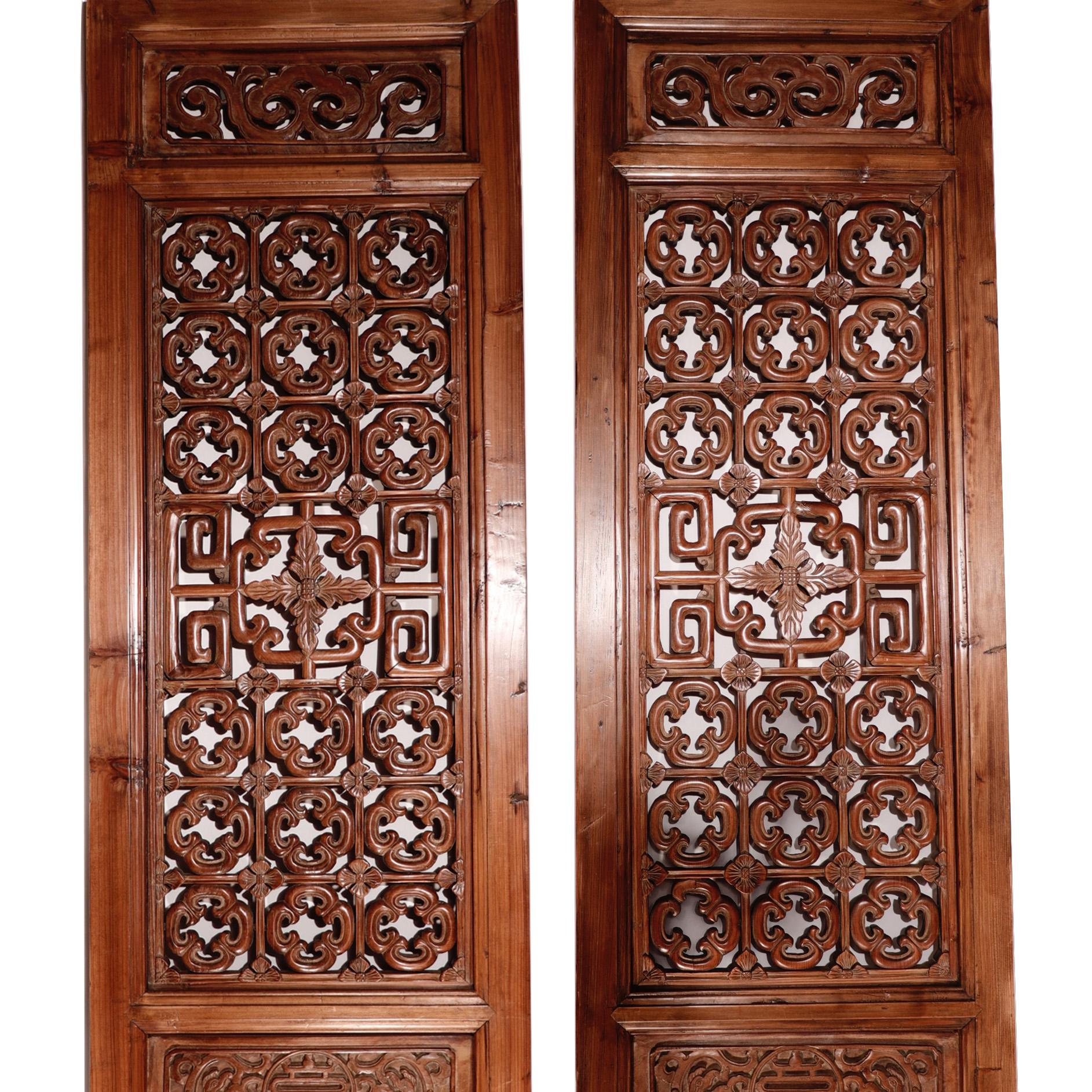 A pair of Chinese door panels, handcrafted of elm and cypress woods using traditional mortise and tenon joinery, having relief carving and an intricate openwork quatrefoil lattice pattern and corner blossoms on each upper section, central small