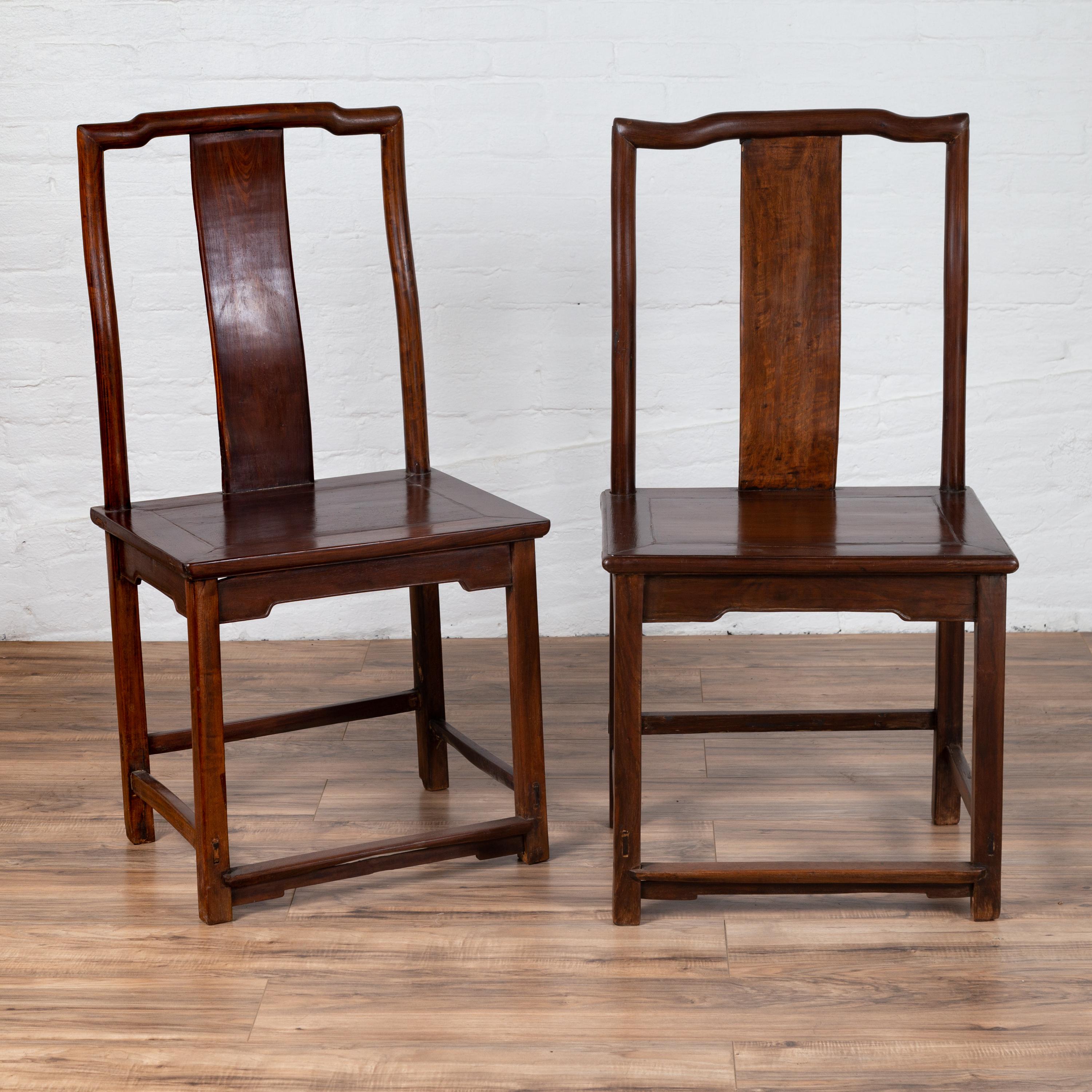 A pair of antique Chinese elmwood scholar's ceremonial chairs from the early 20th century, with dark patina and sinuous back splats. We have several chairs available with slight variations. Contact us for more info. Born in China during the early