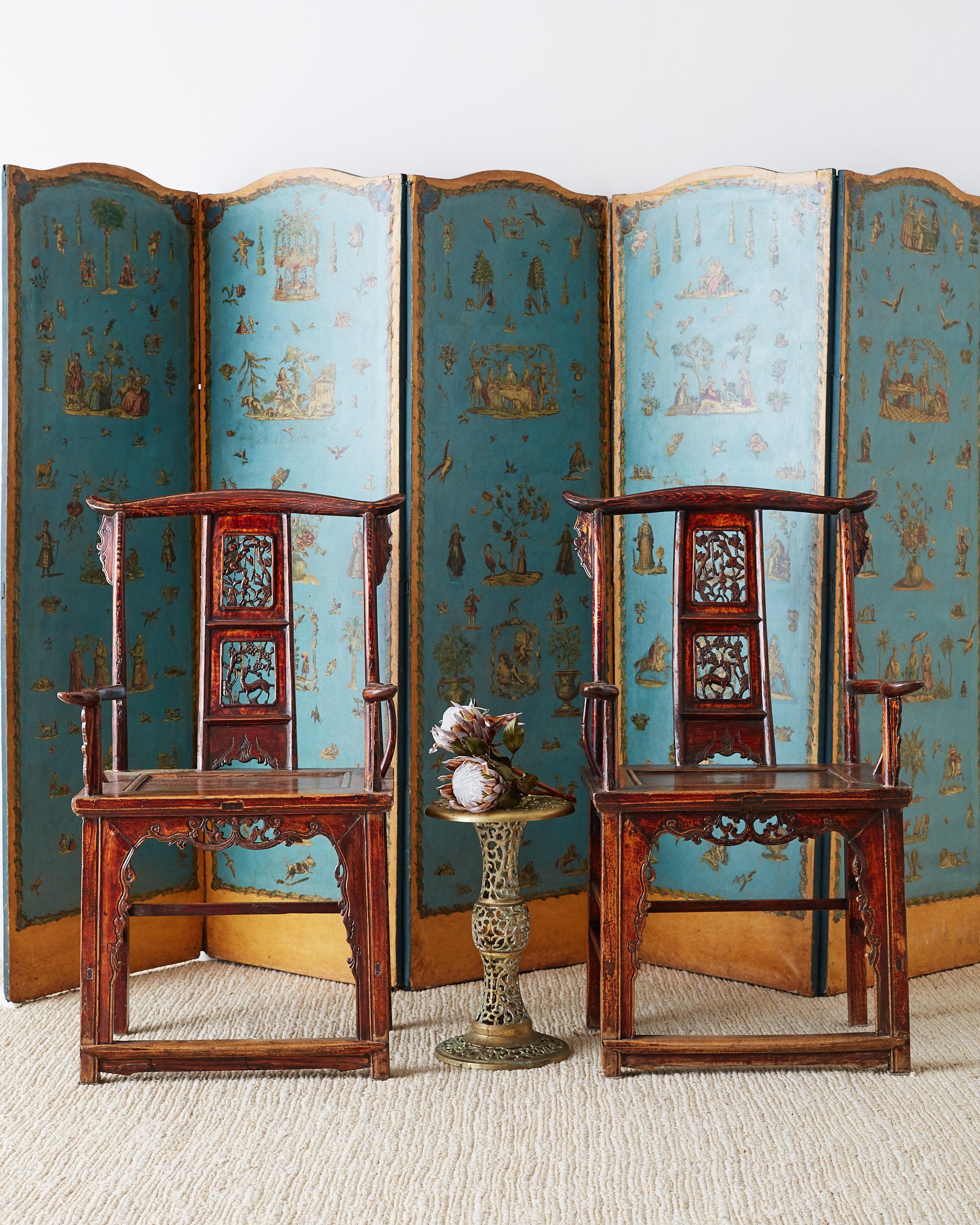 Highly carved pair of Chinese elm yoke back officials hat chairs. Featuring a decorative back splat with figural scenes. The arms have a whimsical serpentine form and the spandrels on the crest and front apron have finely carved detail. Constructed