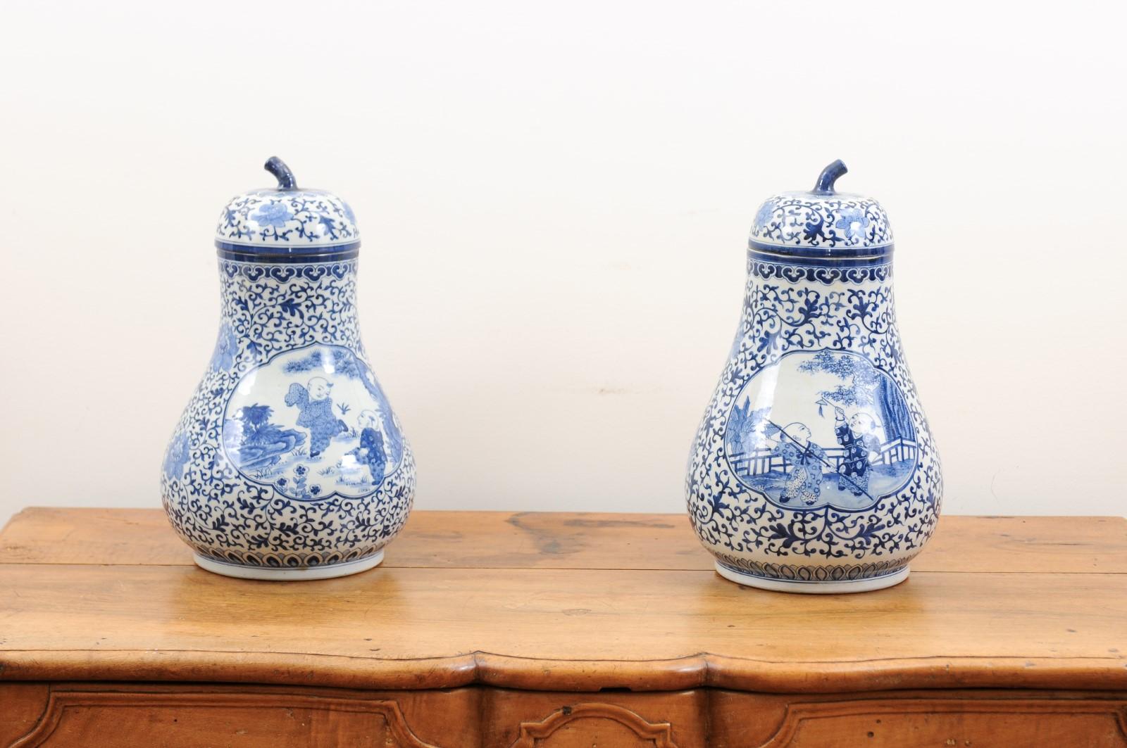 A pair of blue and white Chinese export porcelain vases from the early 20th century, with lids and Chinoiseries scenes. Created in China during the early years of the 20th century, each of this pair of pear-shaped blue and white porcelain vases