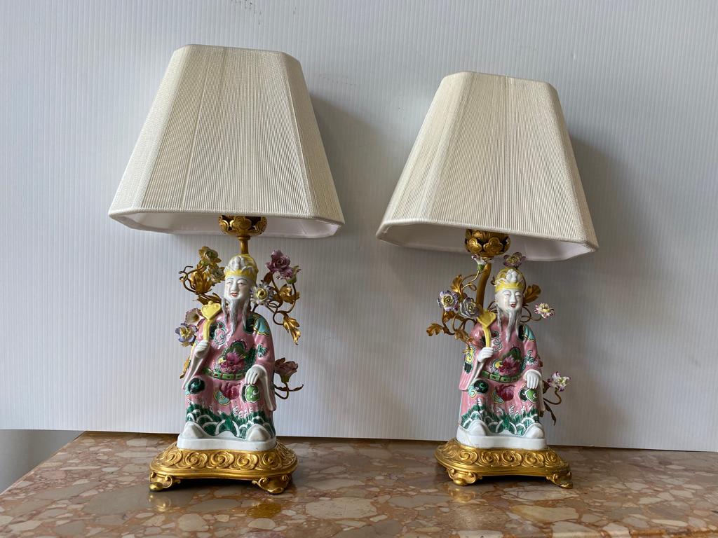 This pair of bonze Dor'a mounted Chinese export lamps depict a Scholar/figure each holding a Ruyi scepters and surrounded by hand made flowers and painted on gold dor'a vines enamel decorated seated figures with dragon robes extra large footed