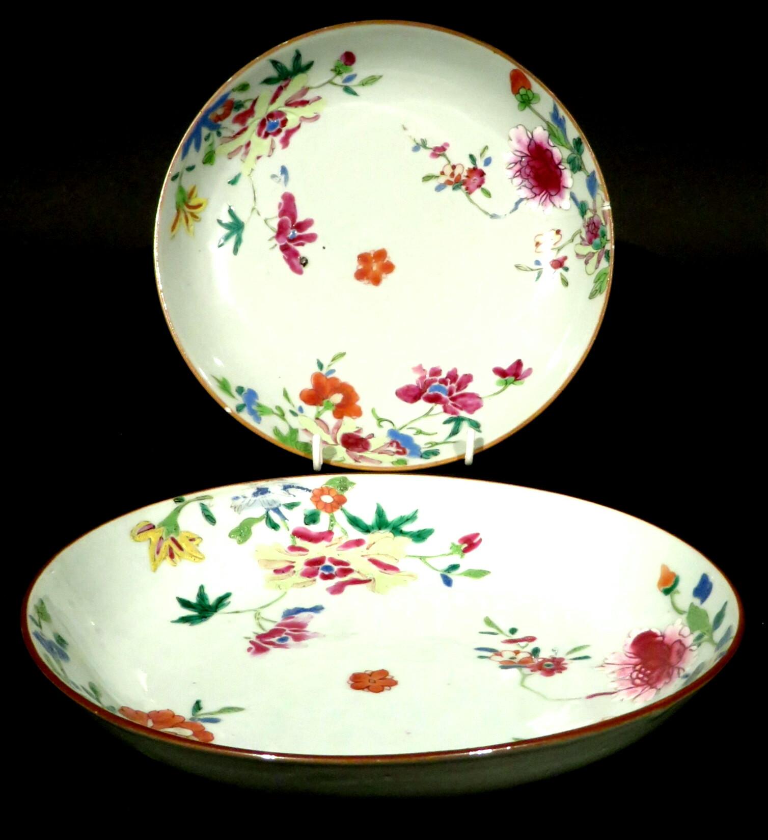 Both saucer-shaped bodies raised on a conforming circular foot, their central fields decorated with a famille rose paellet depicting flower blossoms & foliage, rising up to red oxide edged rims. Both having frits and faint hairline cracks visible on