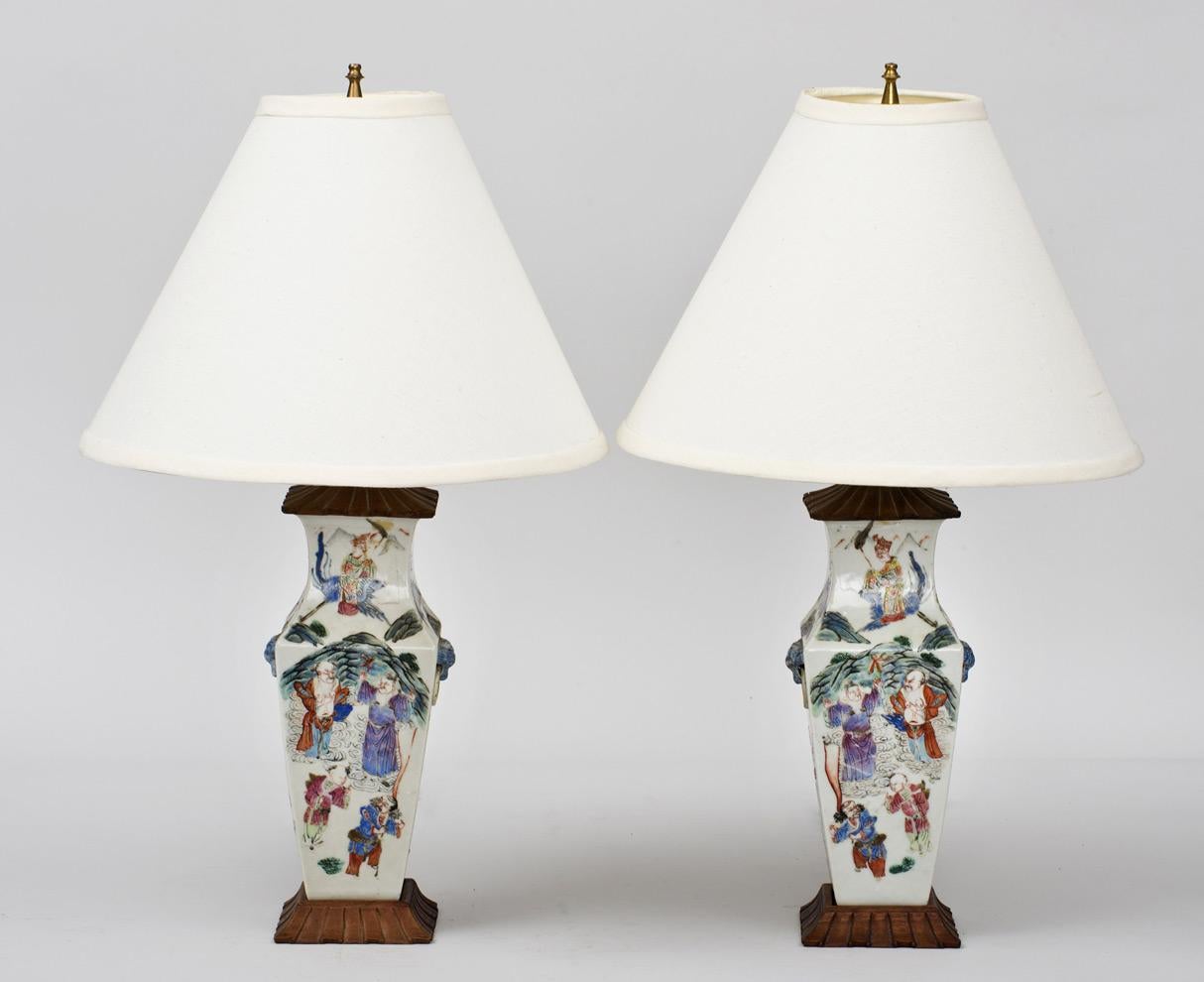 Pair of small Chinese export Famille Rose porcelain square-form baluster vases mounted as lamps, decorated with male figures in various forms of pursuit, with molded mock lion mask and ring handles and carved wooden lids and bases. There is a small