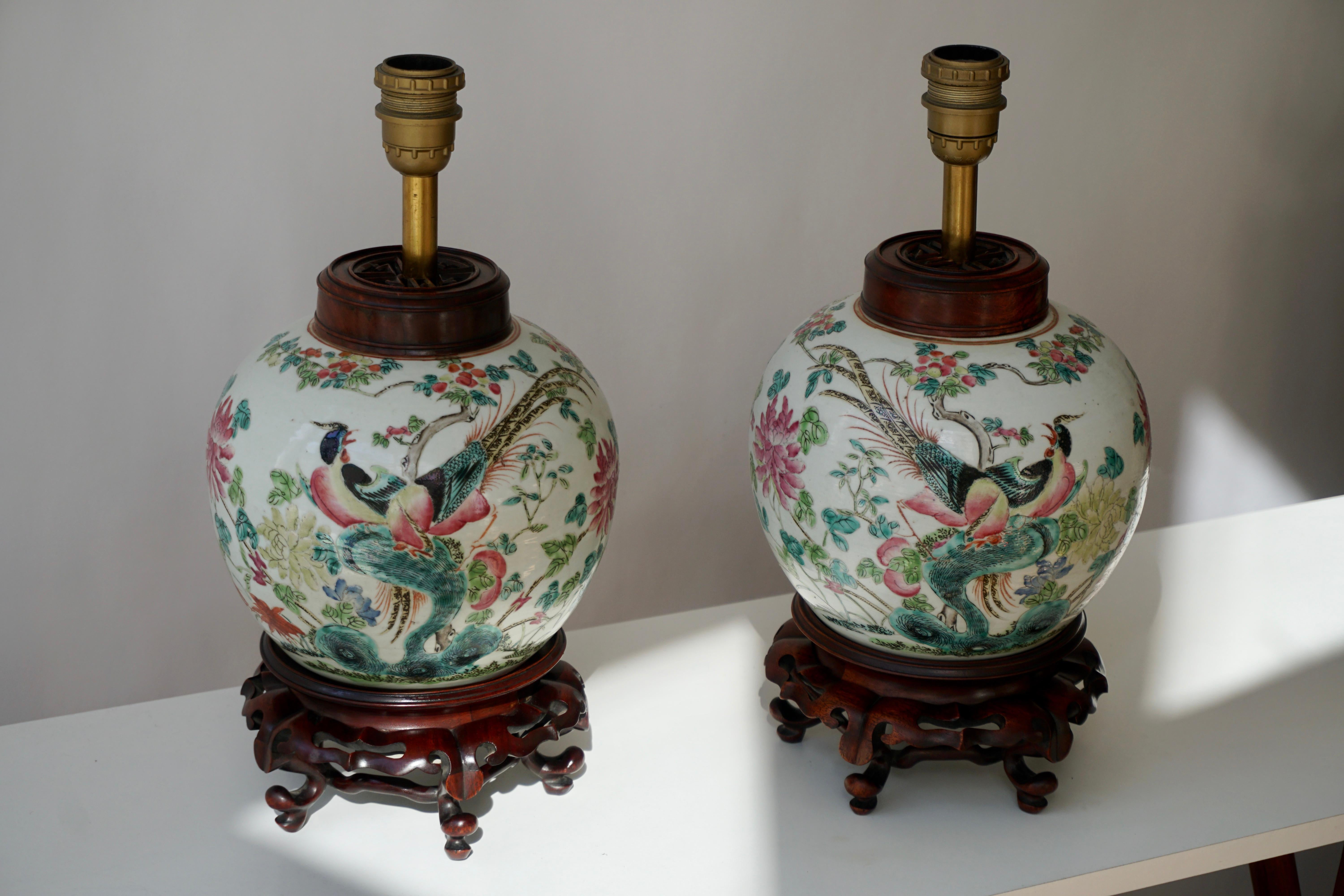 Pair of elegant Chinese porcelain painted table lamps with beautiful colorful hand painted birds, butterflys and flowers. 
Each of these hand painted ginger jars have wooden lids and are mounted as table lamps on a wooden base.
Diameter 21