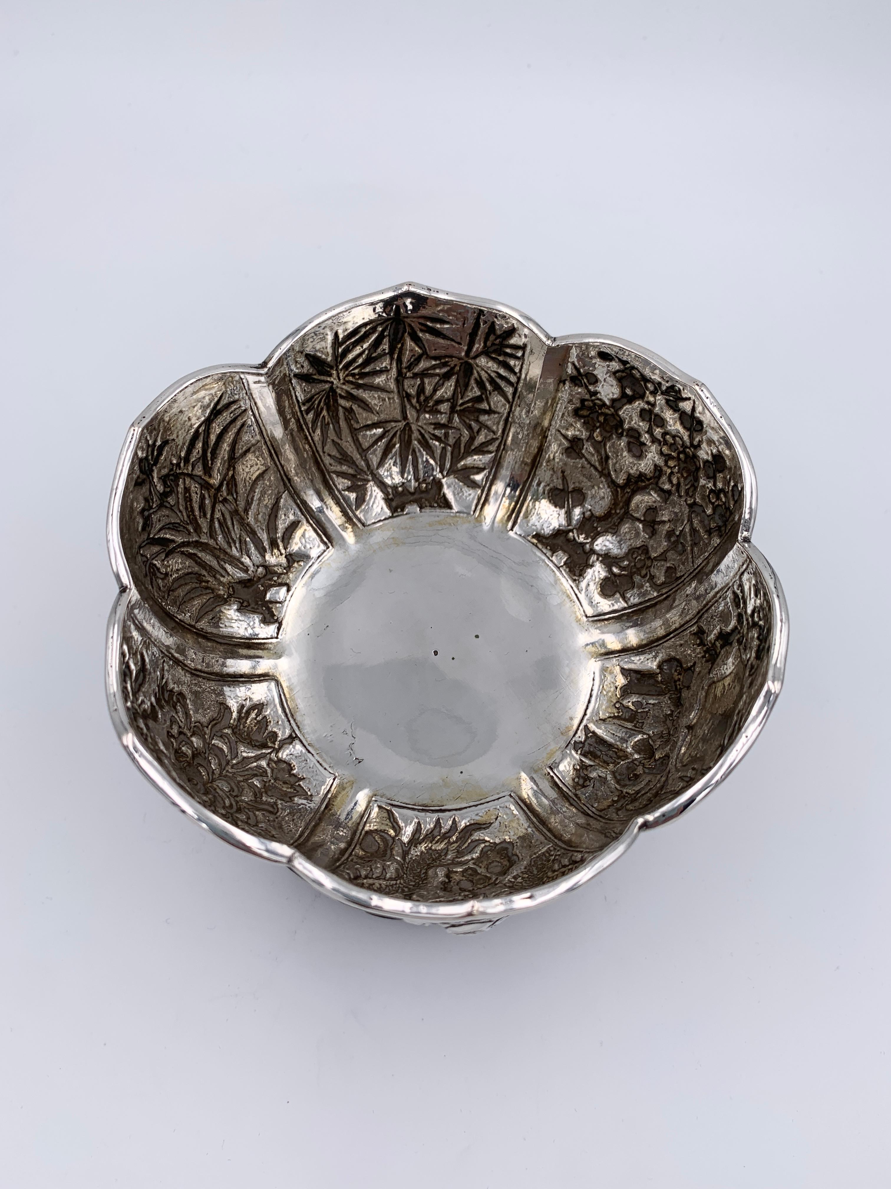 A Pair of Chinese Export Silver Bowls on original wood stands, circa 1880. Both bowls composed of six lotus-shaped panels, sit on a stand with openwork cloud carving. Each panel is embossed and chased, four with plum blossom, orchid, bamboo, and