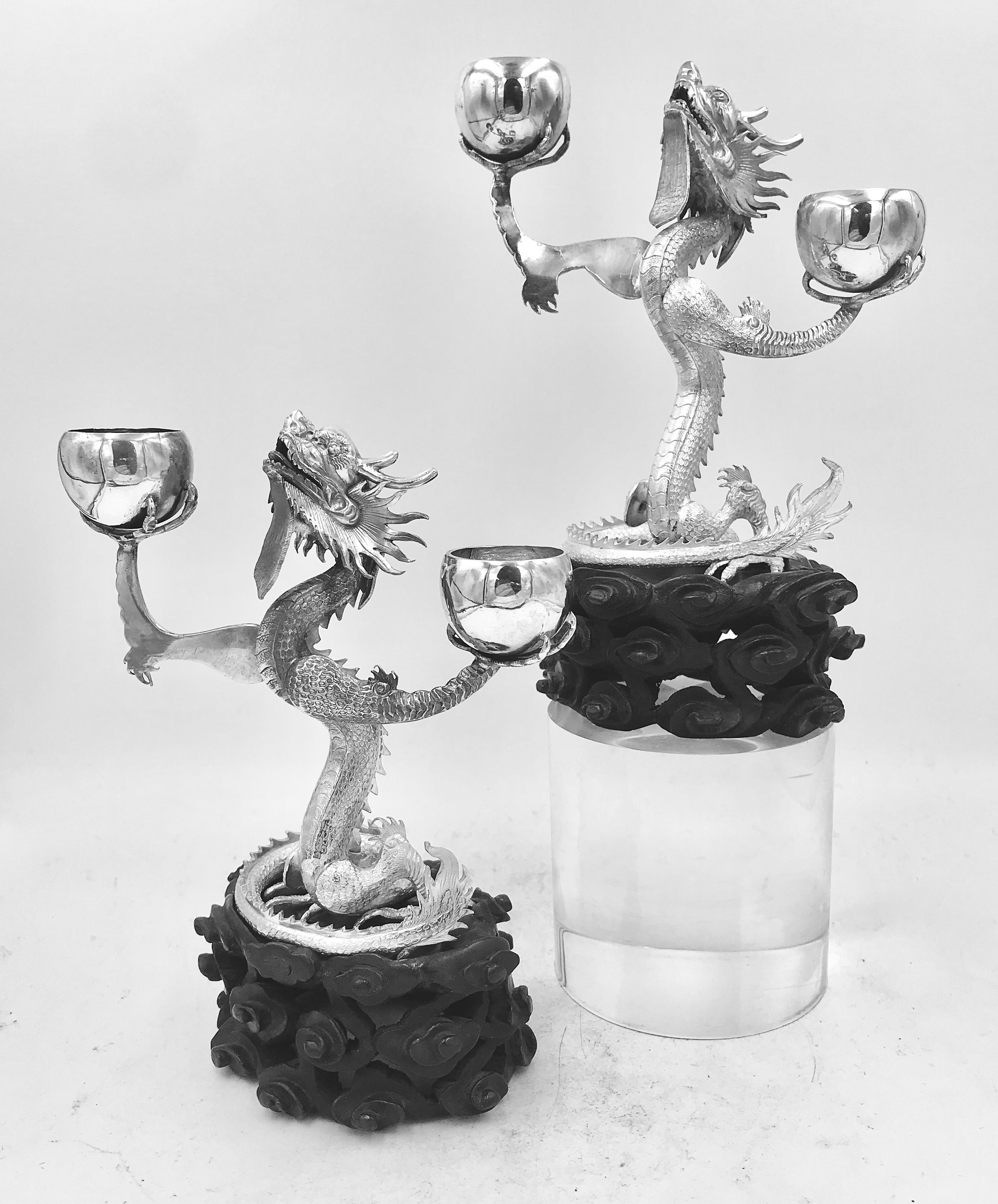 A Pair of Chinese Export Silver Dragon Candelabra, circa 1890. Each finely detailed dragon is coiled on an original wood stand, carved with cloud patterns. They were retailed by the firm of Wang Hing, the largest and most well known business selling