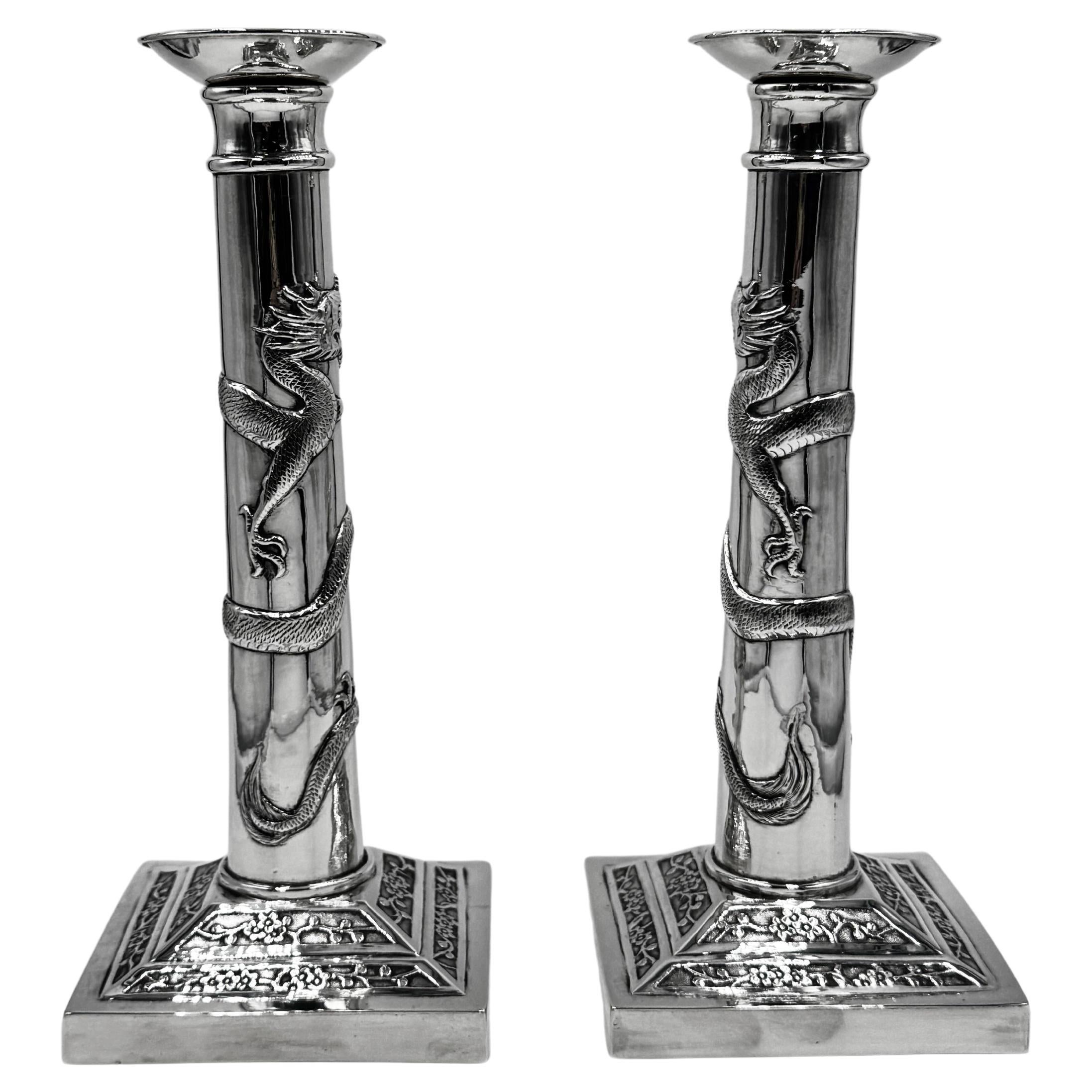 Pareja de candeleros chinos de plata de exportación, cada uno con un dragón enroscado que persigue una perla de fuego alrededor de la columna lisa, con los dragones elevándose en direcciones opuestas para enfrentarse entre sí. Las bases cuadradas