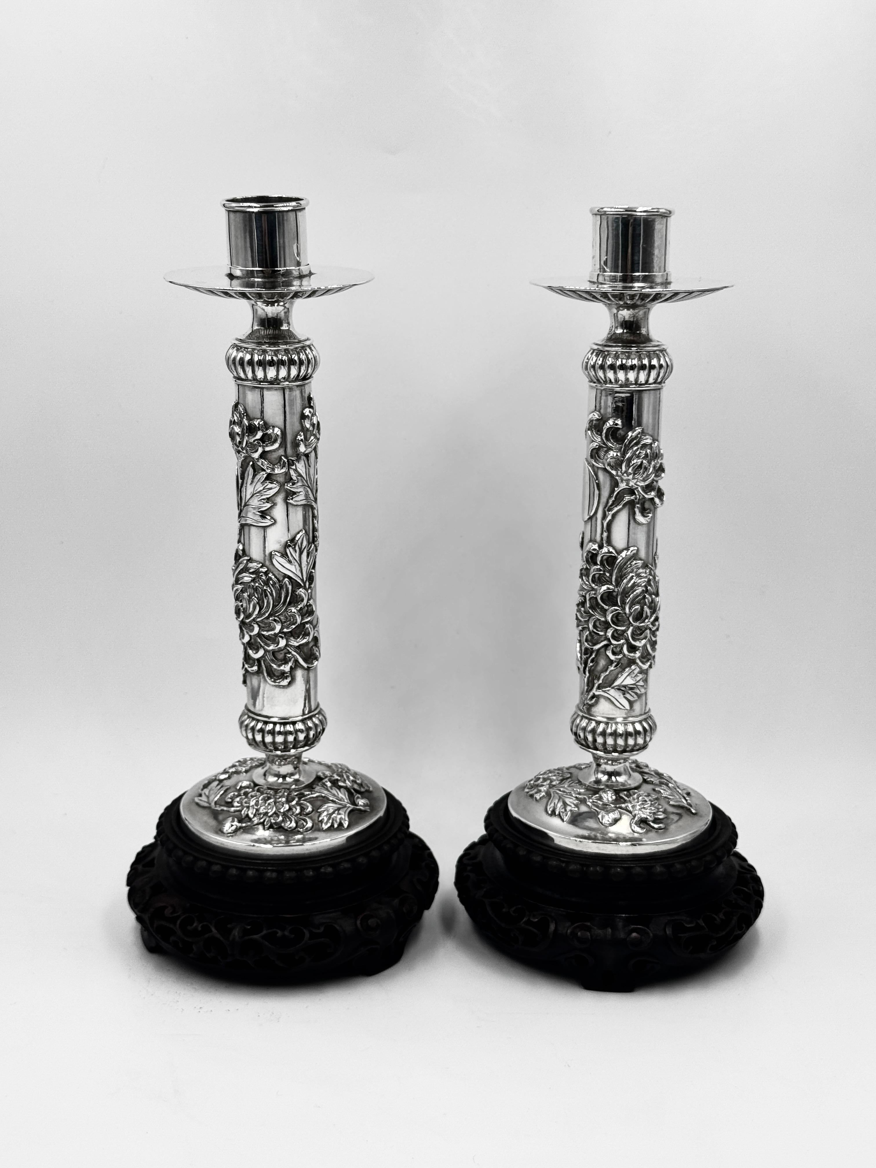 Coppia di candelieri d'argento cinesi da esportazione su supporti originali in legno, Shanghai circa 1885. 
I candelieri presentano una decorazione a crisantemi molto dettagliata intorno al corpo e sulla base. I supporti in legno raffigurano un