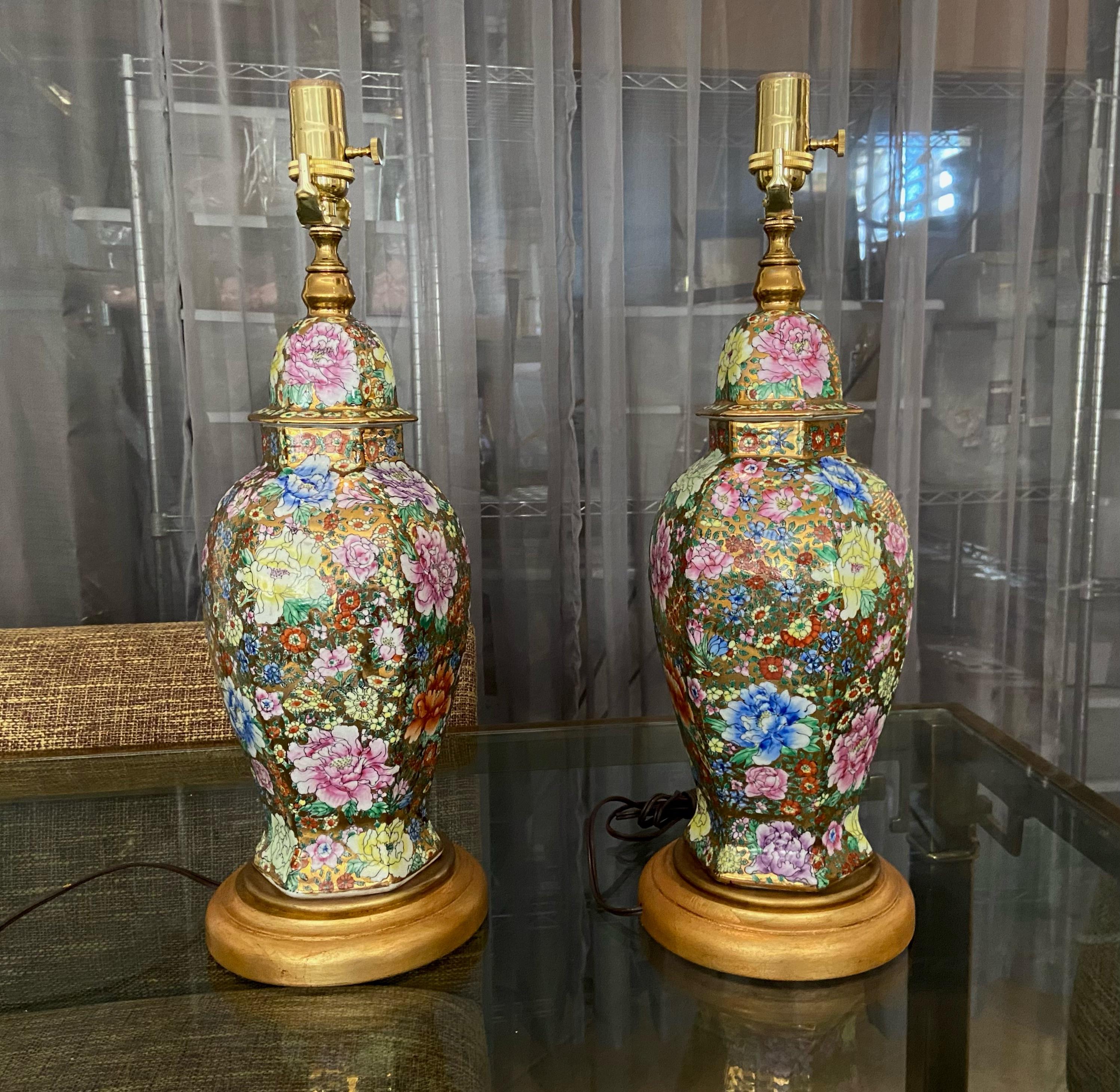 Pair of Chinese porcelain famille rose Millefleurs hexagon shape vases mounted as table lamps on giltwood turned bases. Beautifully crafted with bright applied floral images and 23k gold background accents. Newly wired including new brass fittings