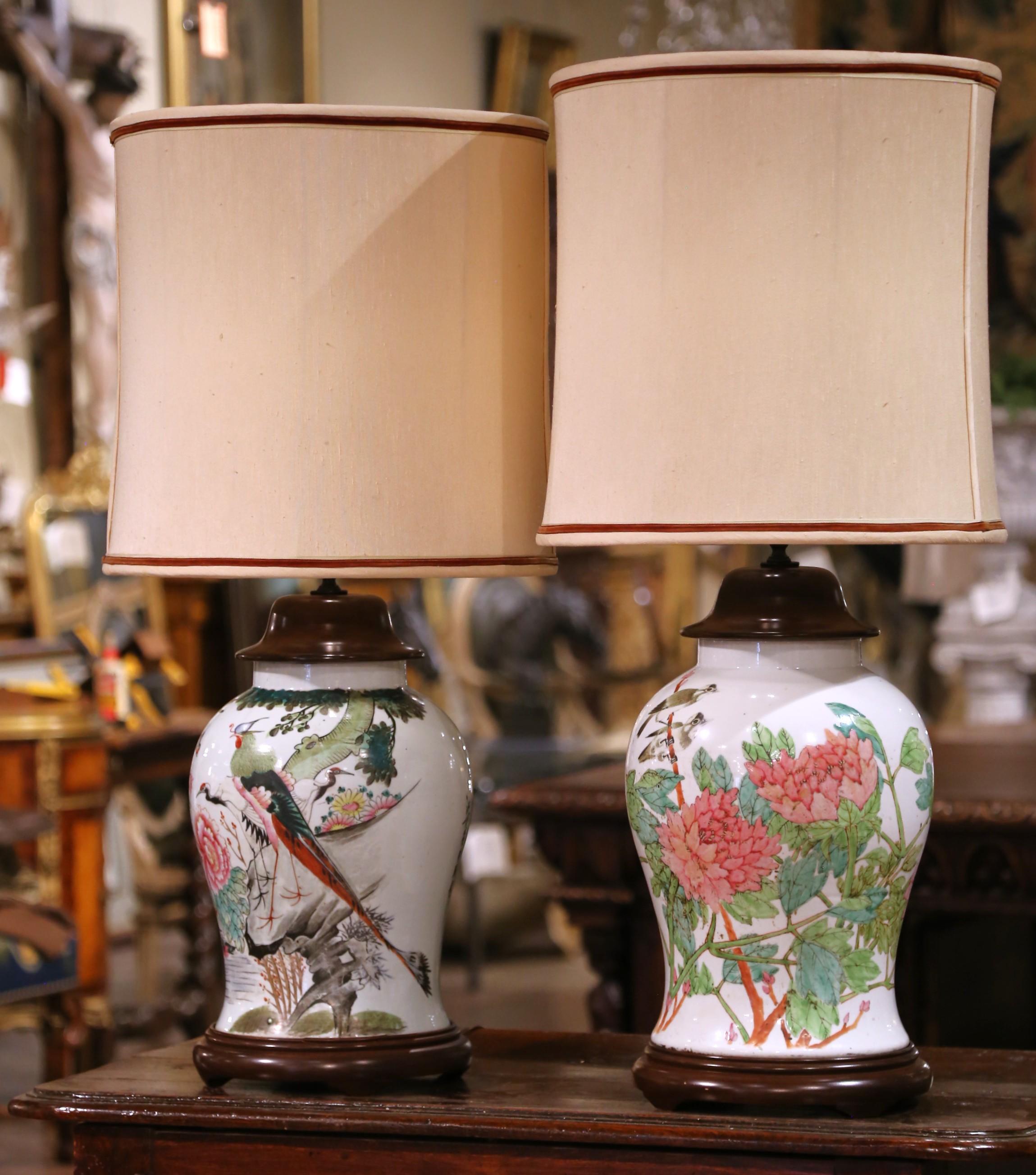 This elegant pair of vintage porcelain lamps was converted from lidded Chinese vase jars, beautifully hand-painted in the Famille Rose palette. Crafted in the mid-20th century, each lamp showcases a vivid tableau of birds perched among flowering