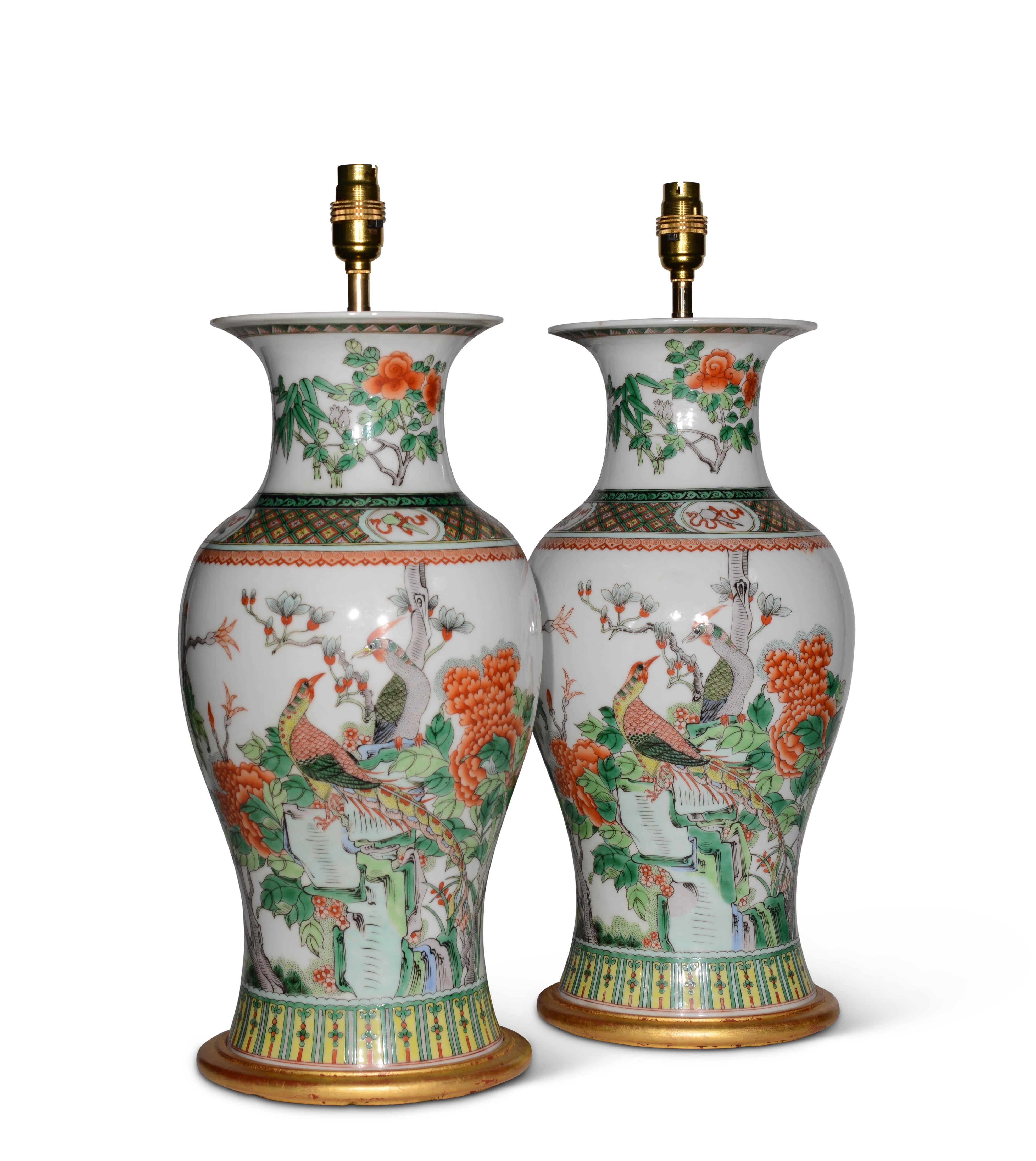 A fine pair of early 20th century Chinese famille verte baluster vases, decorated with exotic birds amongst trees and foliage and rocky outcrops with furthers stylised foliate detailing, predominantly in tones of green on a white background, now