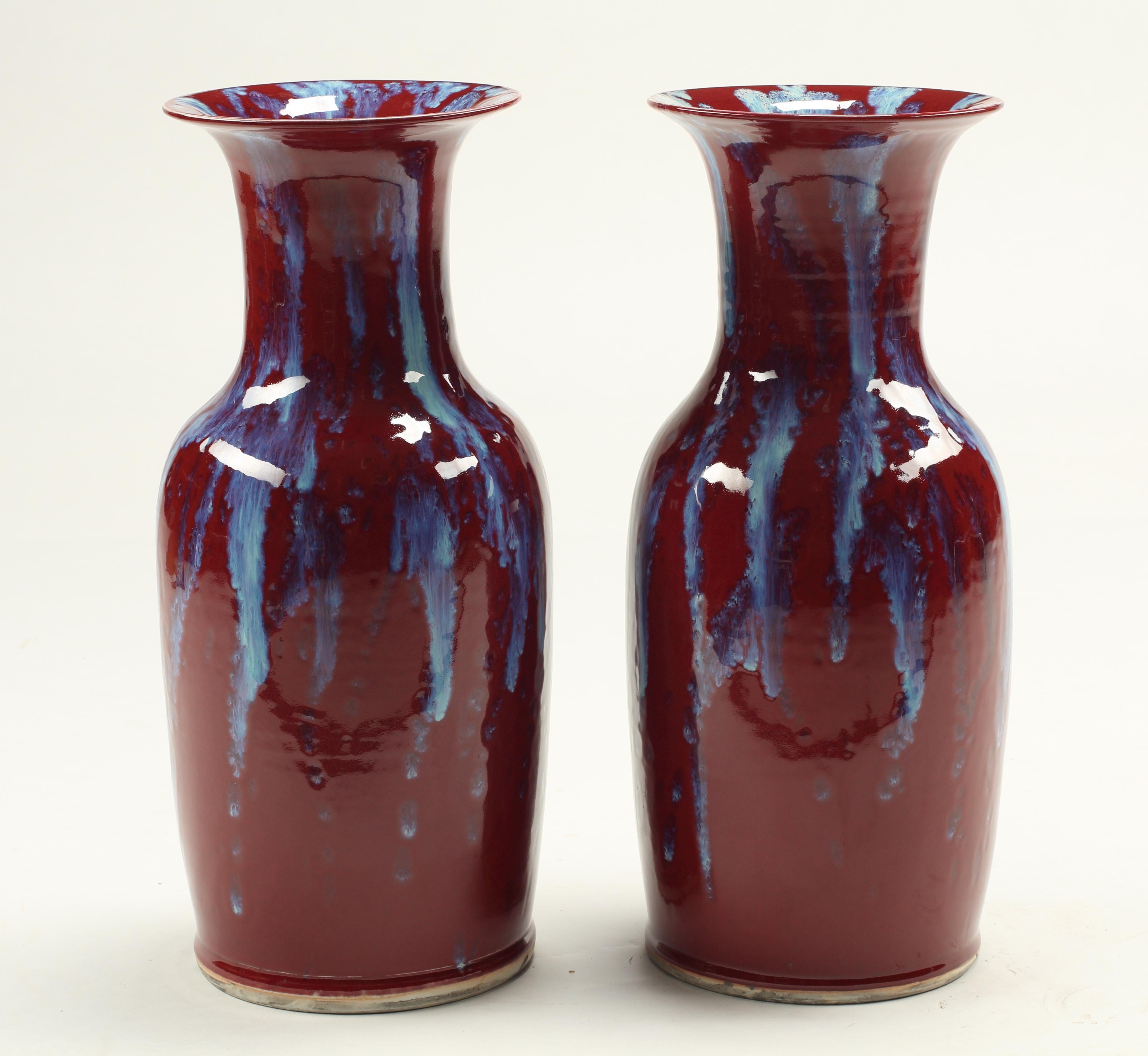 Questa coppia di vasi cinesi in porcellana smaltata flambé mostra la maestria dell'arte ceramica tradizionale. Le profonde tonalità rosso sangue fanno da sfondo a cascate di blu vivo che creano l'effetto ipnotico di una fiamma che gocciola. La