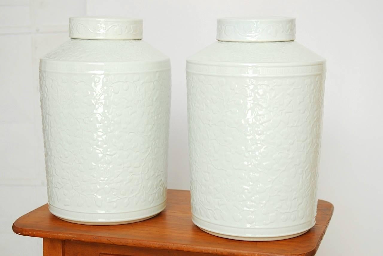 Large pair of Chinese blanc de chine lidded jars or vases featuring a floral blossom motif decorated body. These large vases have a cylindrical shape with matching lids. Beautifully glazed with a soft, raised finish and decorative bands of Greek key