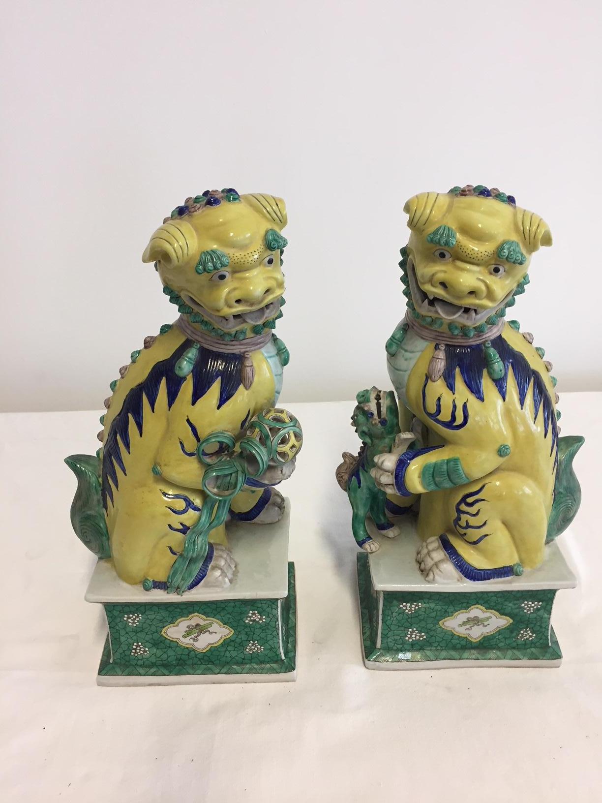 Pair of Chinese Foo dogs and painted stands, perfect condition, glazed hand painted porcelain in color yellow and celadon green and few high lights in color blue, beautiful details: male with ball, female with baby Foo dog.