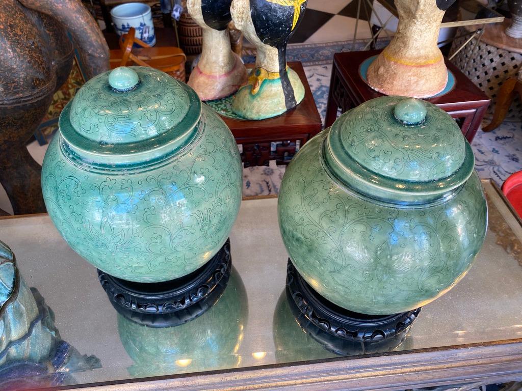 Pair of Chinese ceramic green glazed vessels/jars with original lids having a design of lotus, birds and vines hand carved into the jar itself. The jars have a 