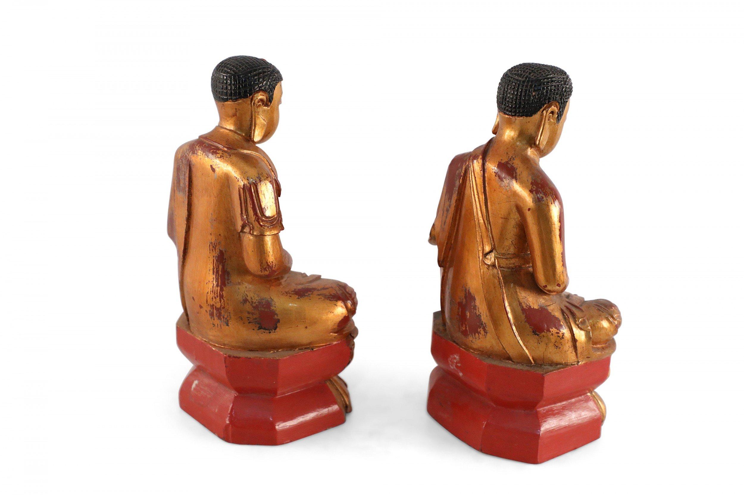 Paar chinesische goldene, geschnitzte Buddha-Figuren aus Holz, die auf floralen und roten Sockeln sitzen (PREIS FÜR Pärchen).
 