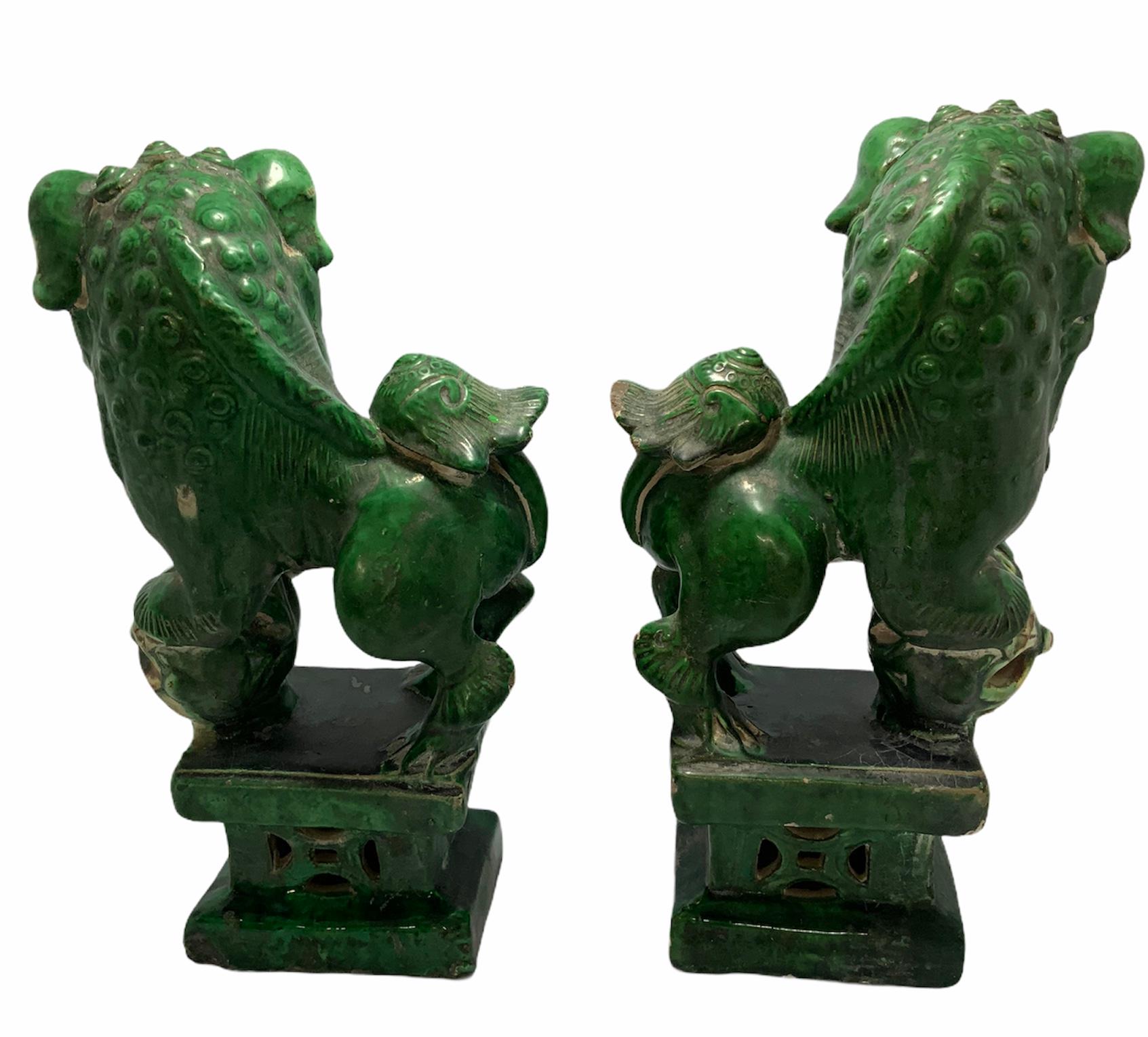 These are two medium size and heavy ceramic Chinese sculptures of foo dogs that are playing with a ball that sounds like bells. They are hand painted green, yellow, and brown color. In Chinese culture foo dogs are lions that represent the yin