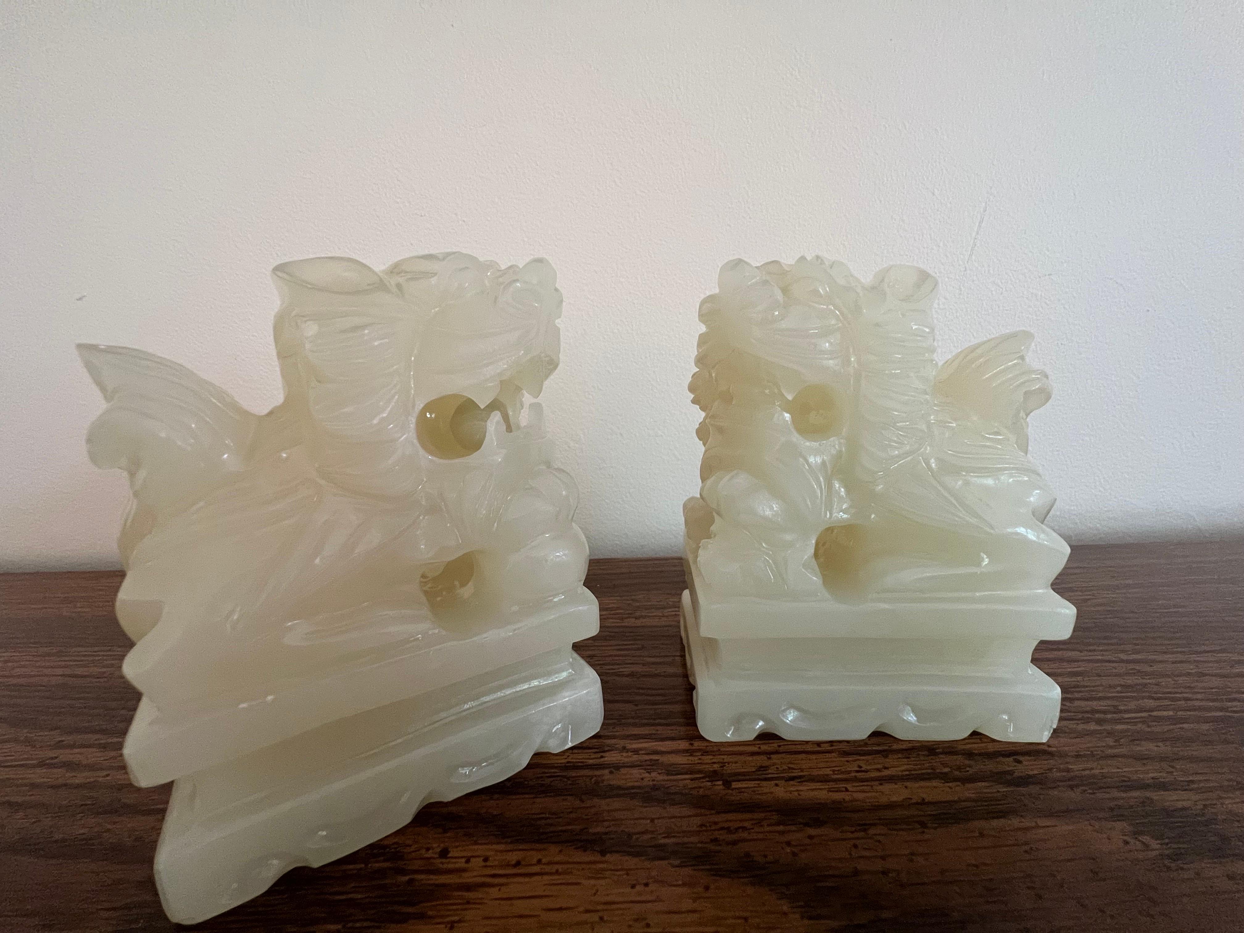 A finely hand-carved pair of Chinese white jade foo dogs or foo lions. One figure has a ball in his mouth, the ball is believed to represent the union of Heaven and Earth. For centuries, the foo dog has been a Feng Shui symbol of protection. These