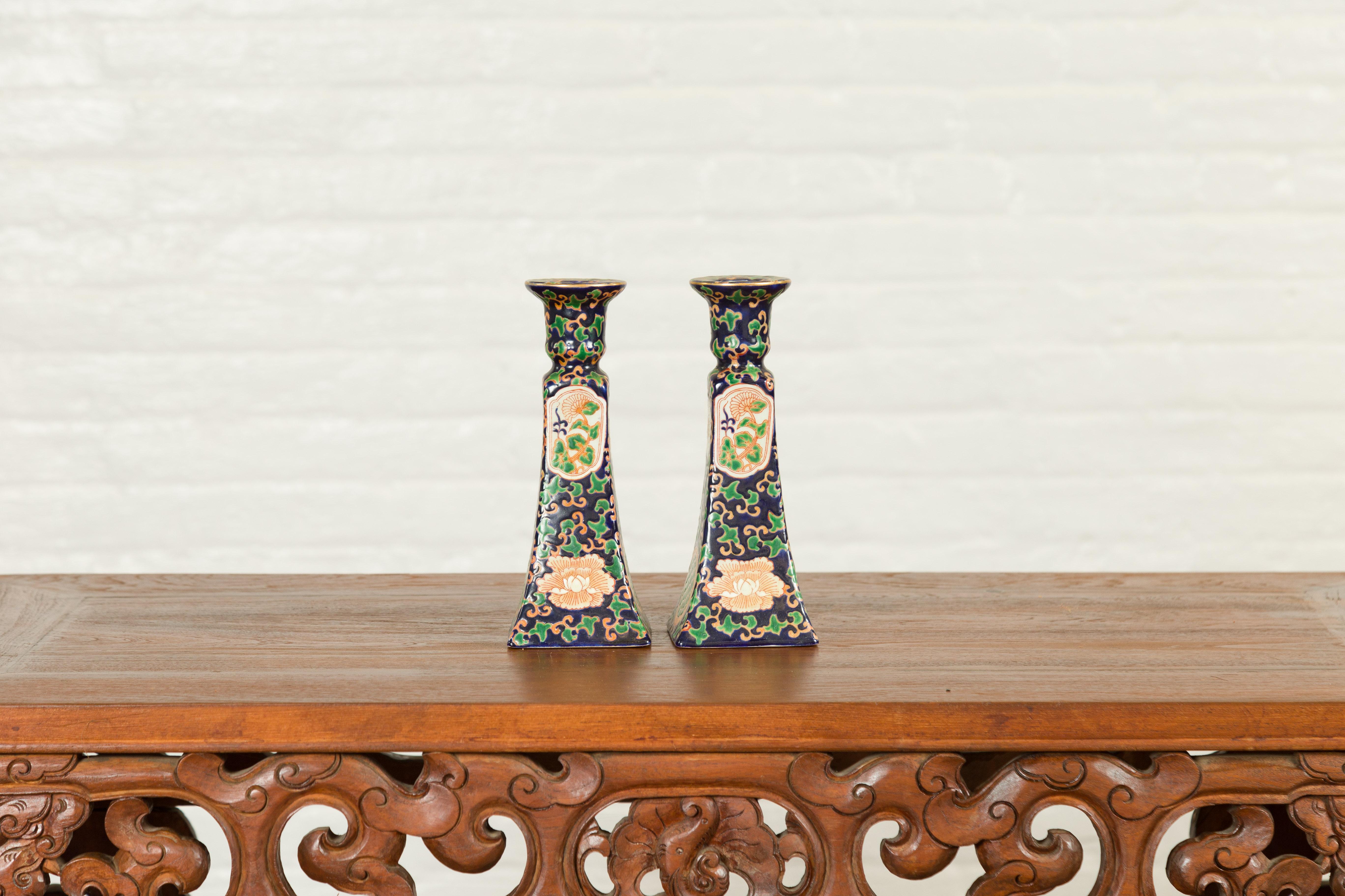 A pair of Chinese contemporary hand painted candlesticks with cobalt blue ground, green and orange floral decor. Charming us with their graceful motifs, each of this pair of Chinese hand painted candlesticks features a cobalt blue ground accented