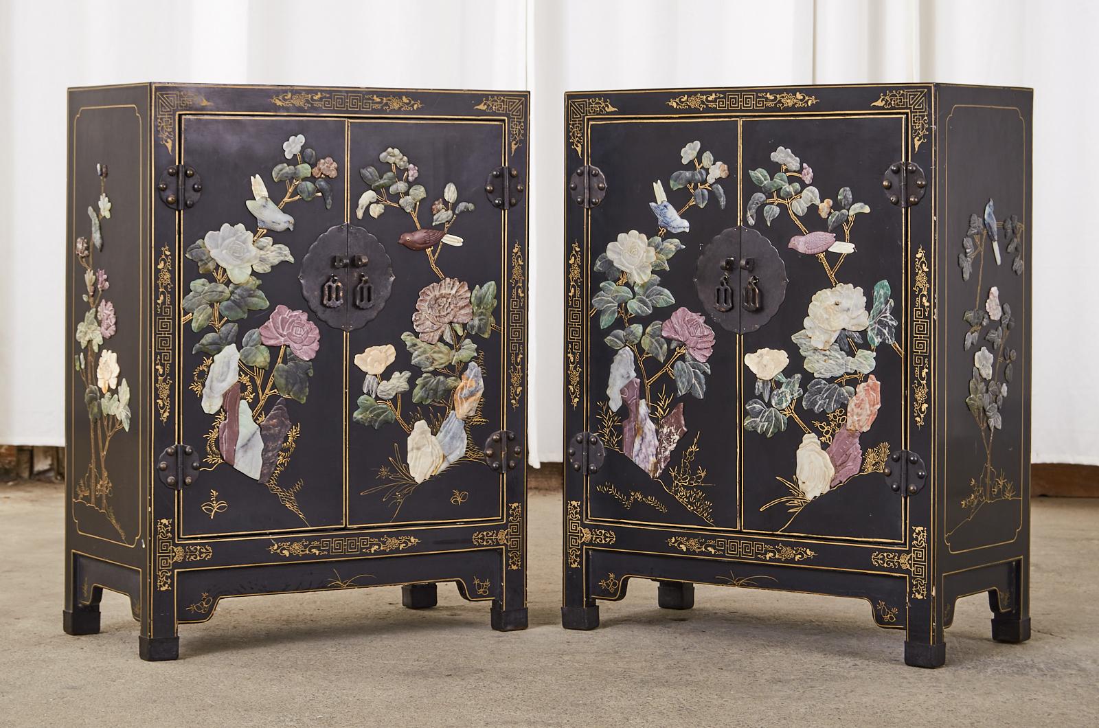 Exquisite pair of Chinese export lacquered cabinets or nightstands decorated with hardstone and soapstone hand carvings of flora and fauna. The chests are matching in size and fronted by two doors with patinated brass metal lockplates and hardware.